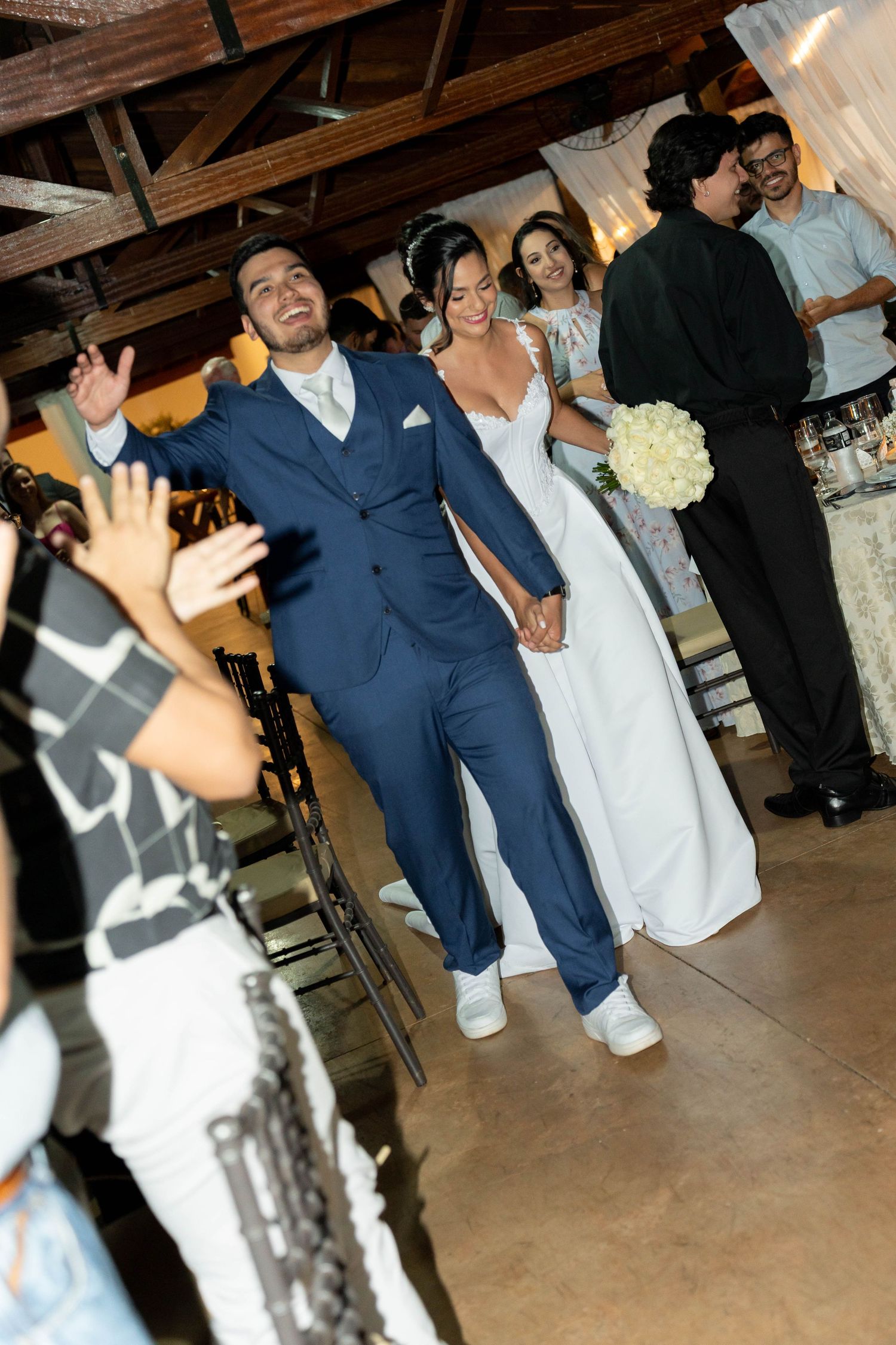 Bride and groom walk hand in hand down the aisle, smiling and waving at guests in a warmly lit wedding venue.
