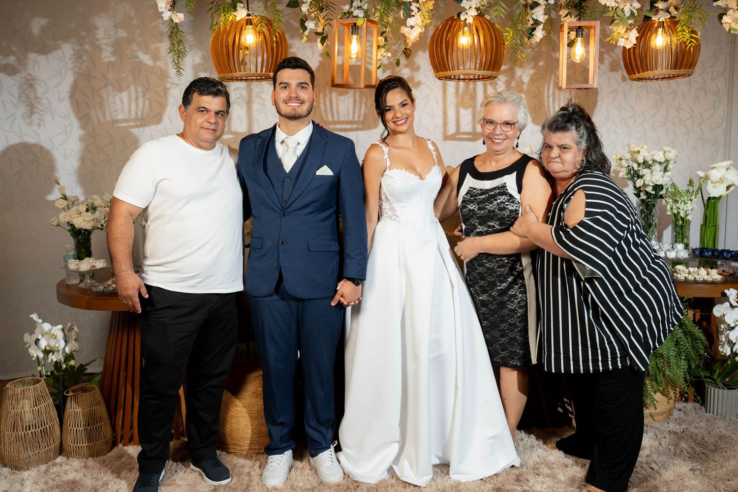A bride and groom pose with three family members at an elegant wedding reception with warm golden lighting.
