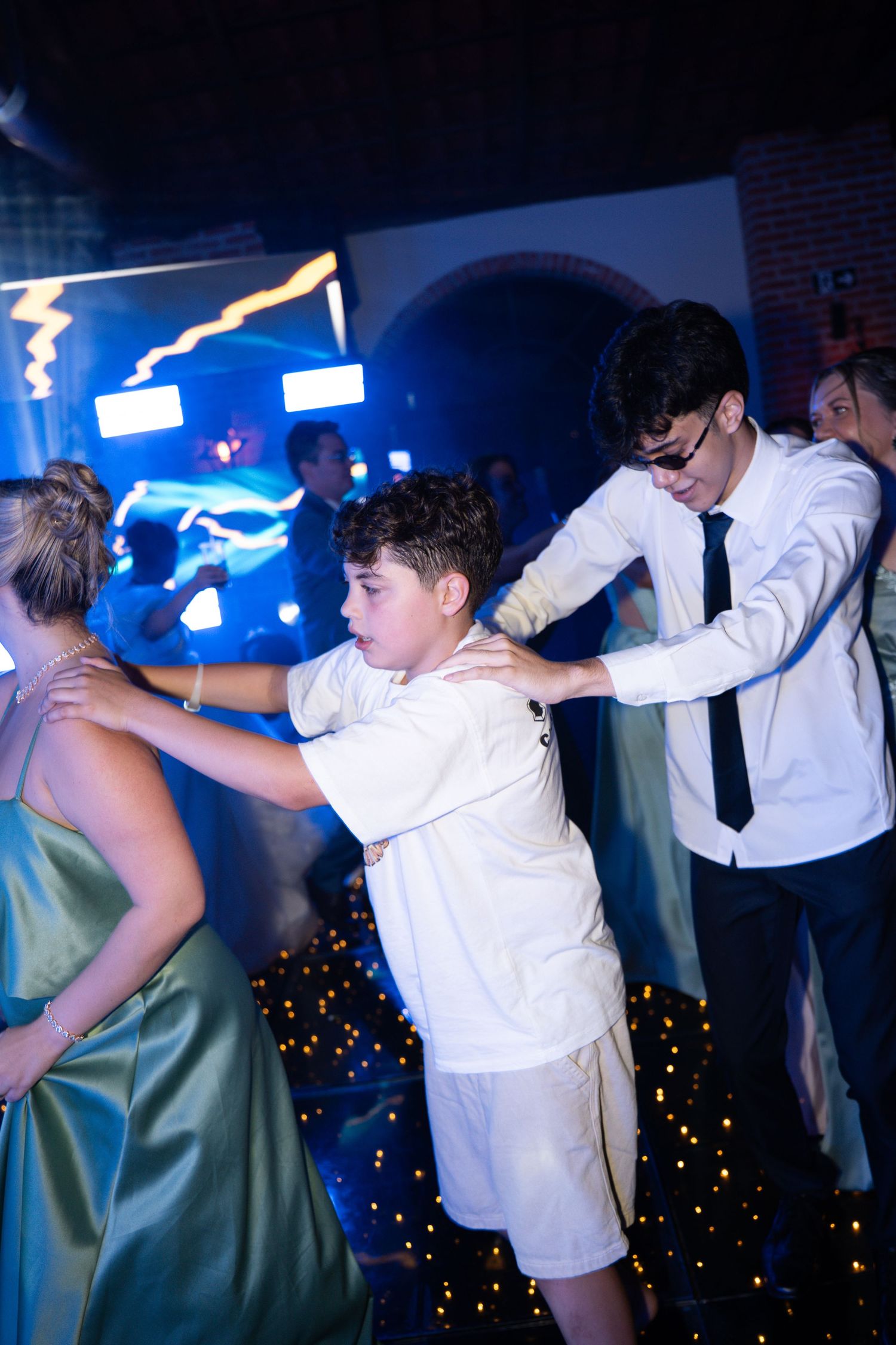 Teens dancing at a formal event under blue lights on a sparkly dance floor.