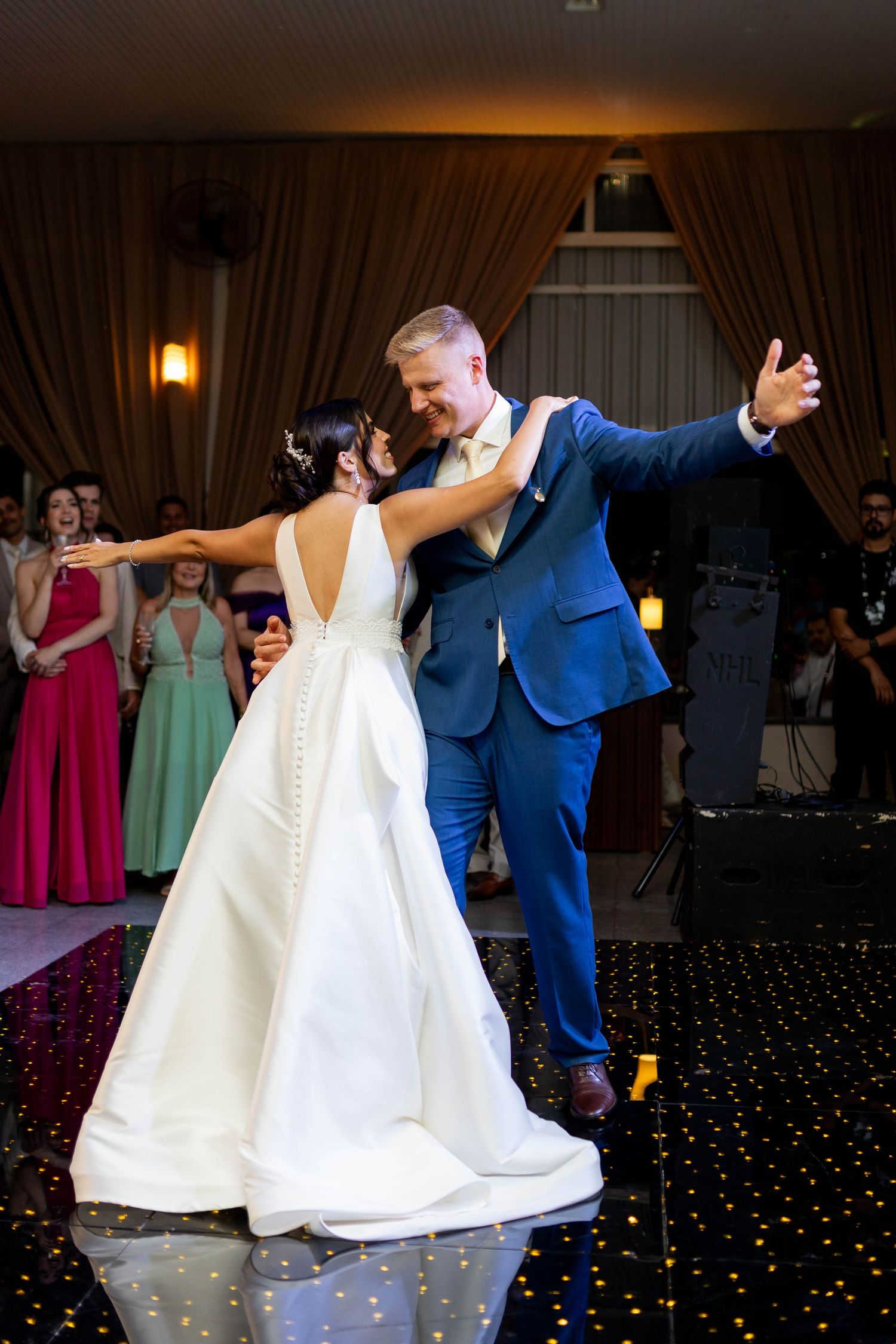 Bride and groom share their first dance at wedding reception, bride in white gown, groom in blue suit.