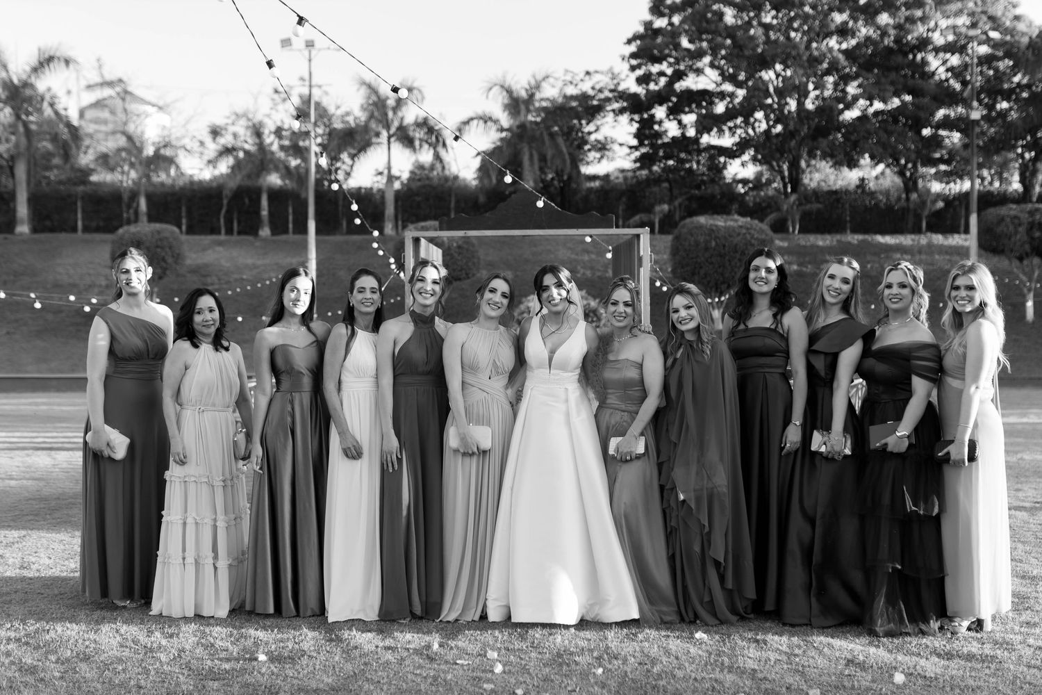 Black and white photo of a bride in white gown posing with bridesmaids in elegant dresses outdoors.