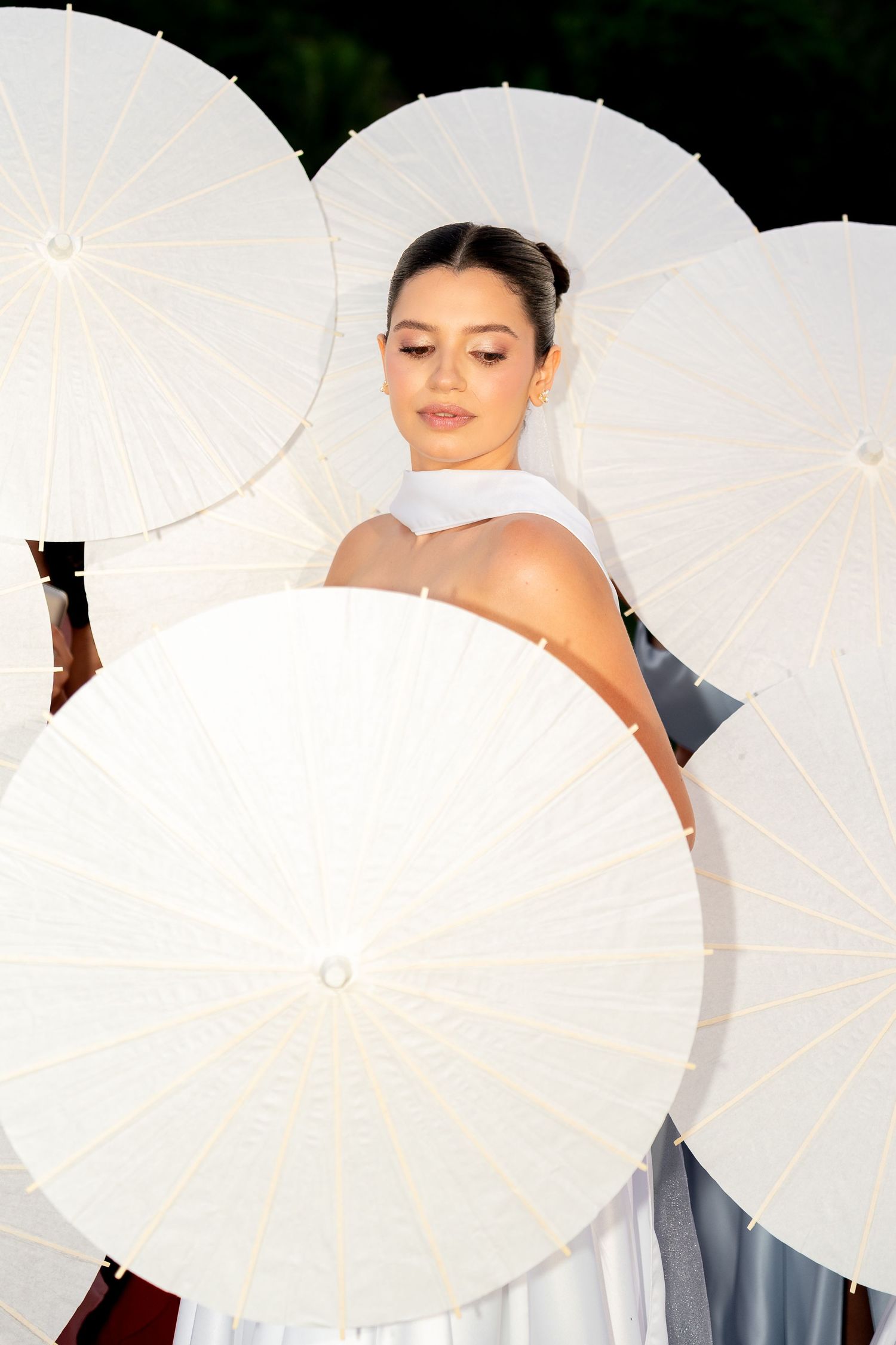 Elegant bride surrounded by multiple white paper parasols in an outdoor wedding setting.