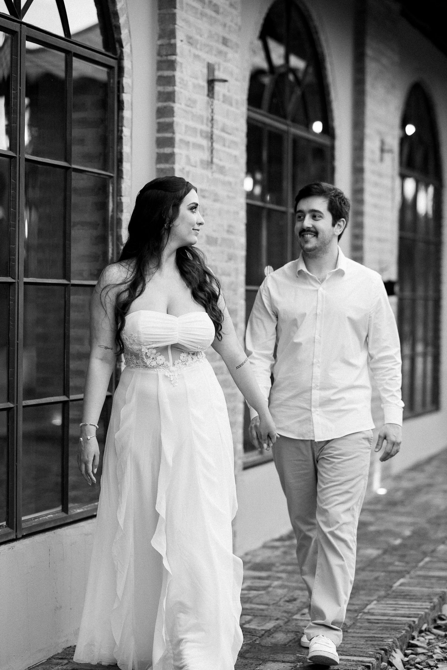 Black and white photo of bride and groom walking hand in hand outside brick building.