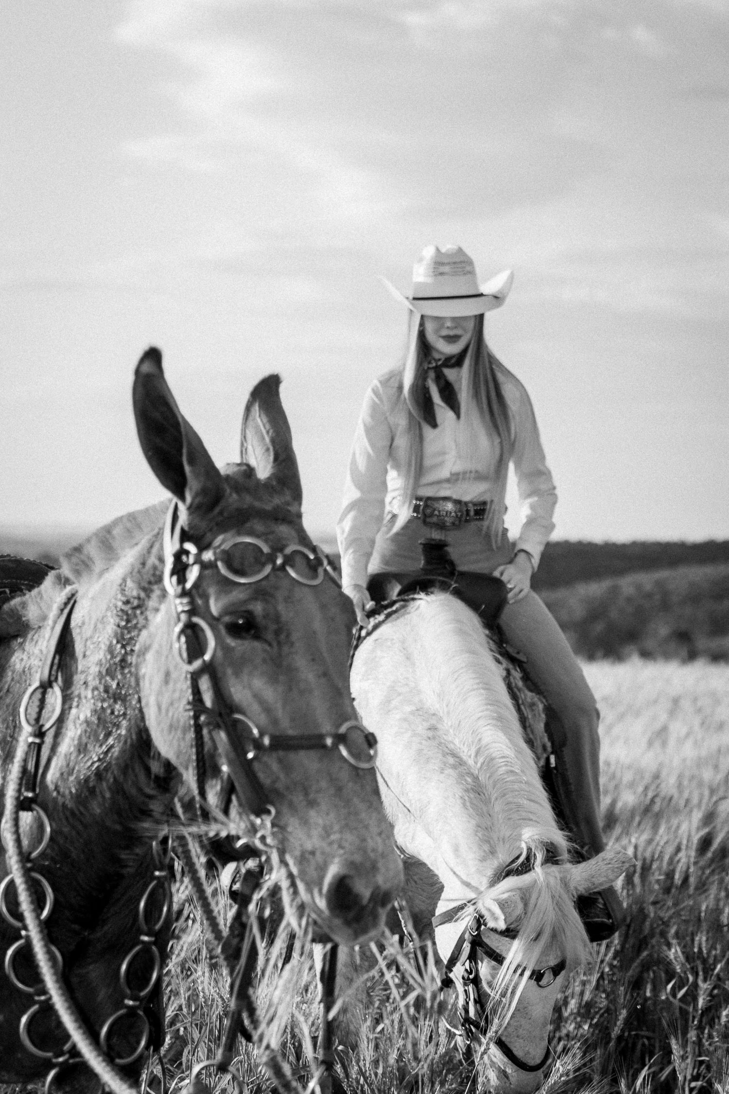 Black and white photo of a cowgirl in white hat riding a horse through a field.