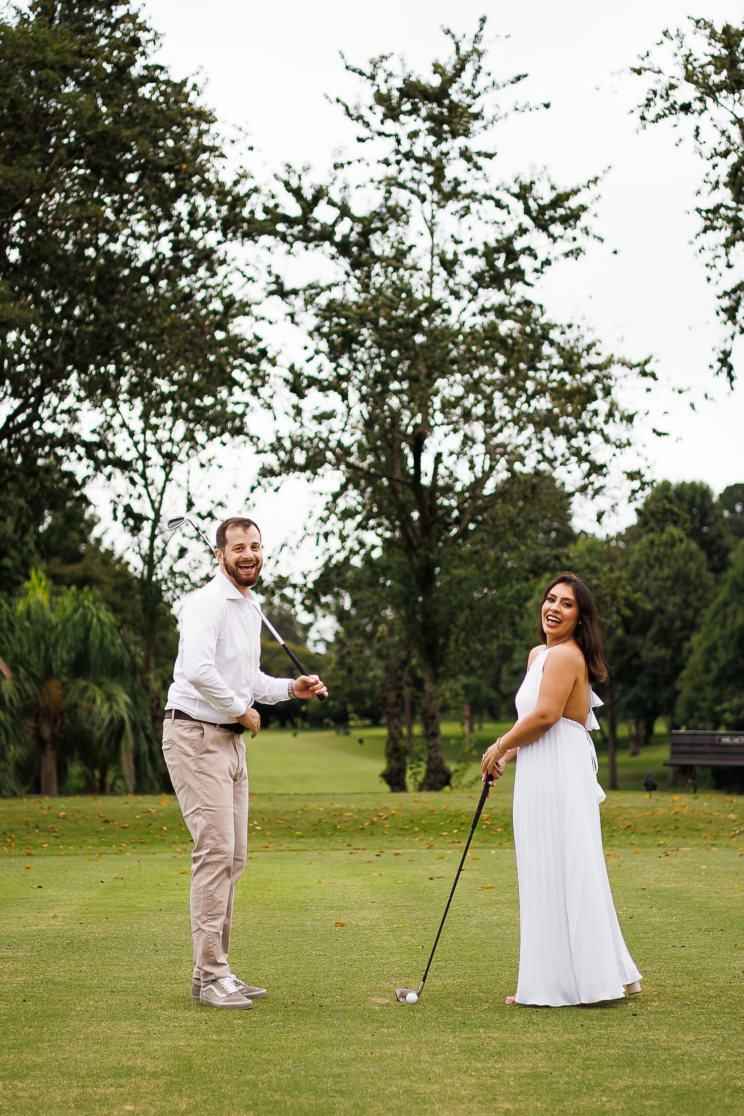 Couple in white attire playing golf on a lush green course, smiling and posing with a golf club.