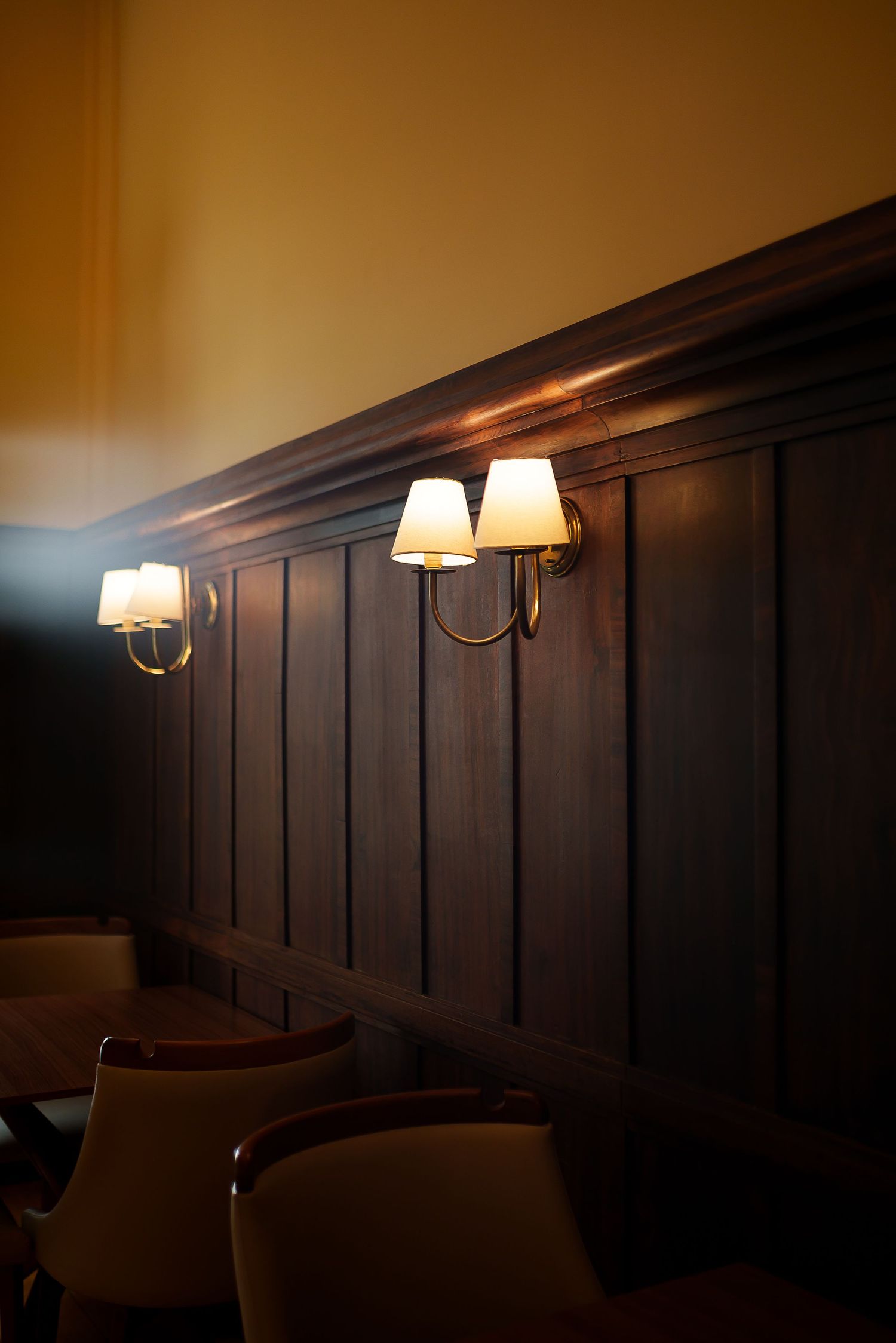 Elegant restaurant interior with dark wood paneling and warm brass wall sconces with white shades illuminating dining chairs.
