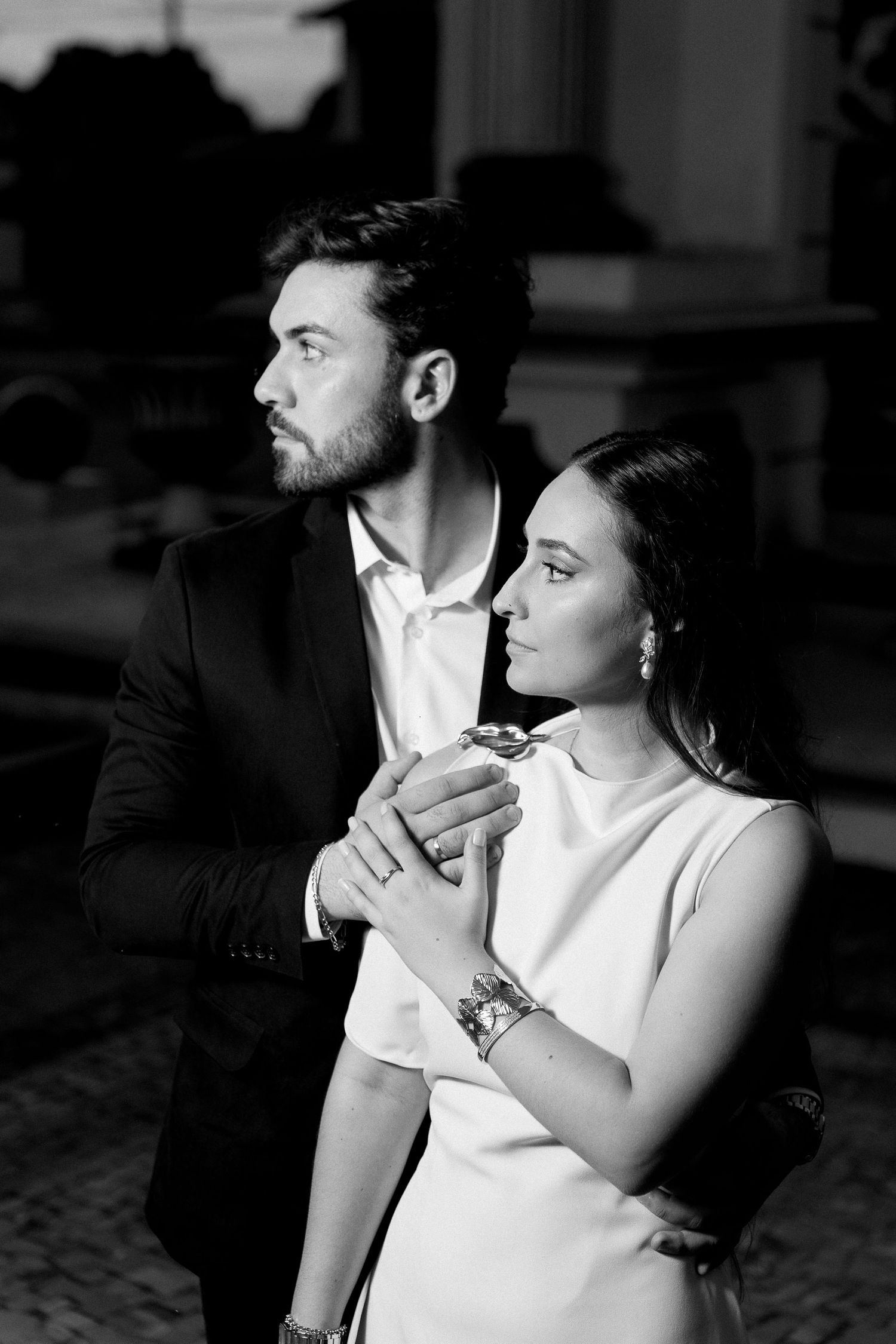 Black and white photo of an elegant couple in formal wear holding hands and gazing into the distance.
