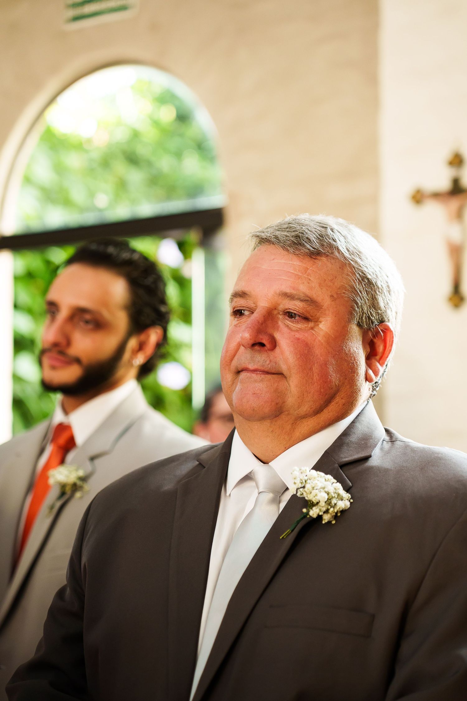 Emotional father of the bride in gray suit with boutonniere at wedding ceremony in church.