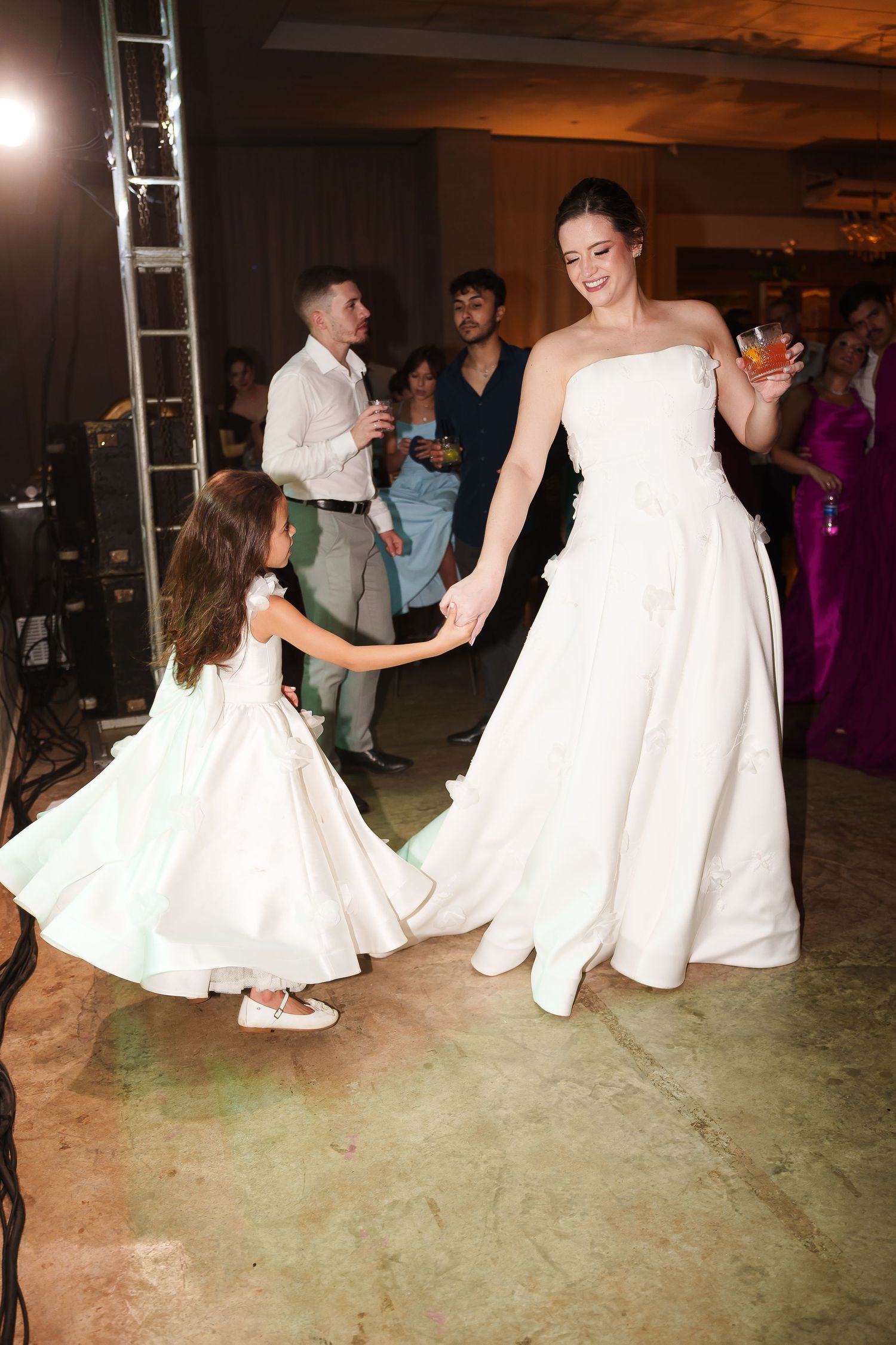 Bride in white strapless gown dancing with flower girl at wedding reception.