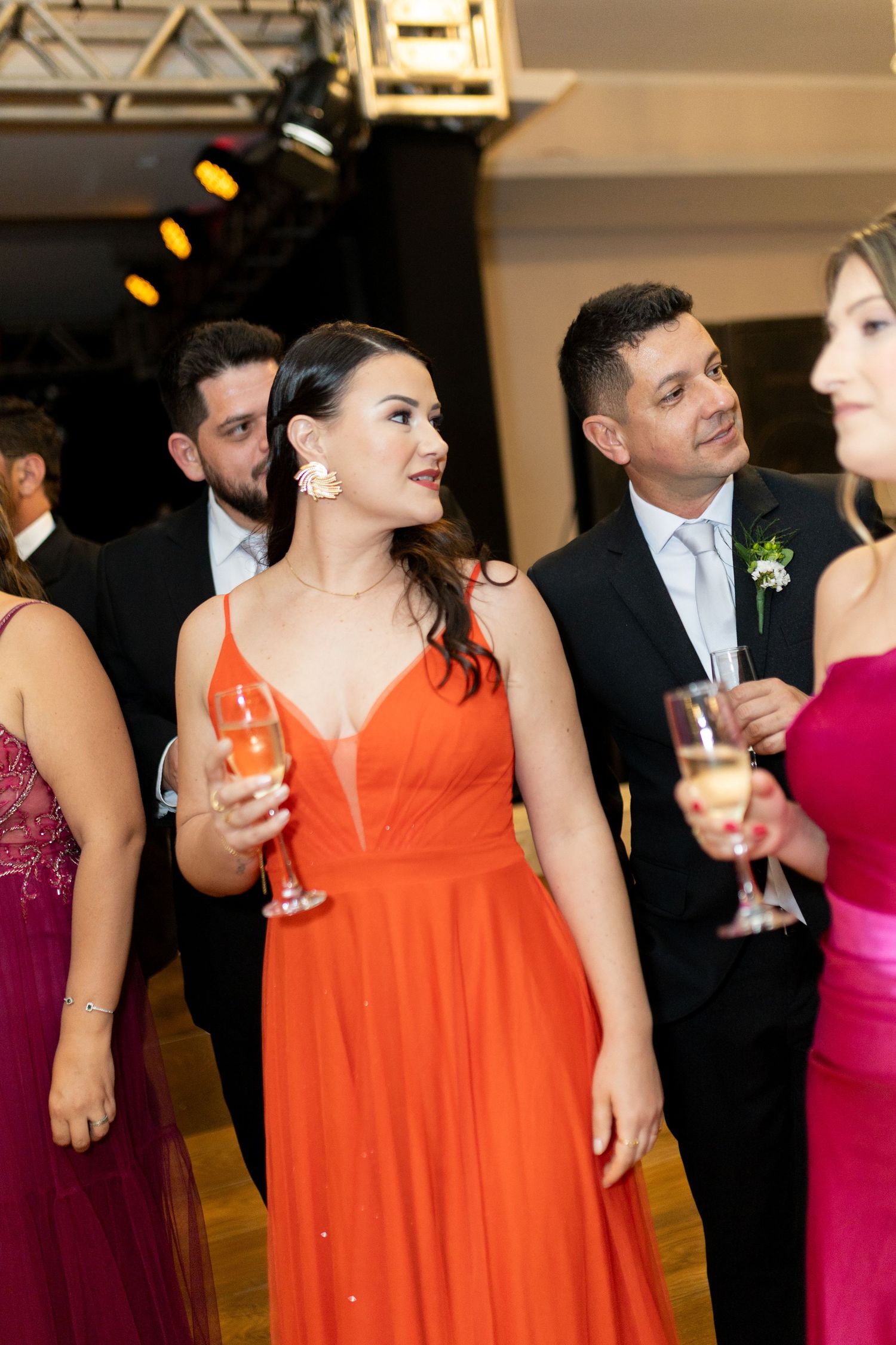 Elegant guests in formal attire holding champagne glasses at a wedding reception, woman in orange gown.