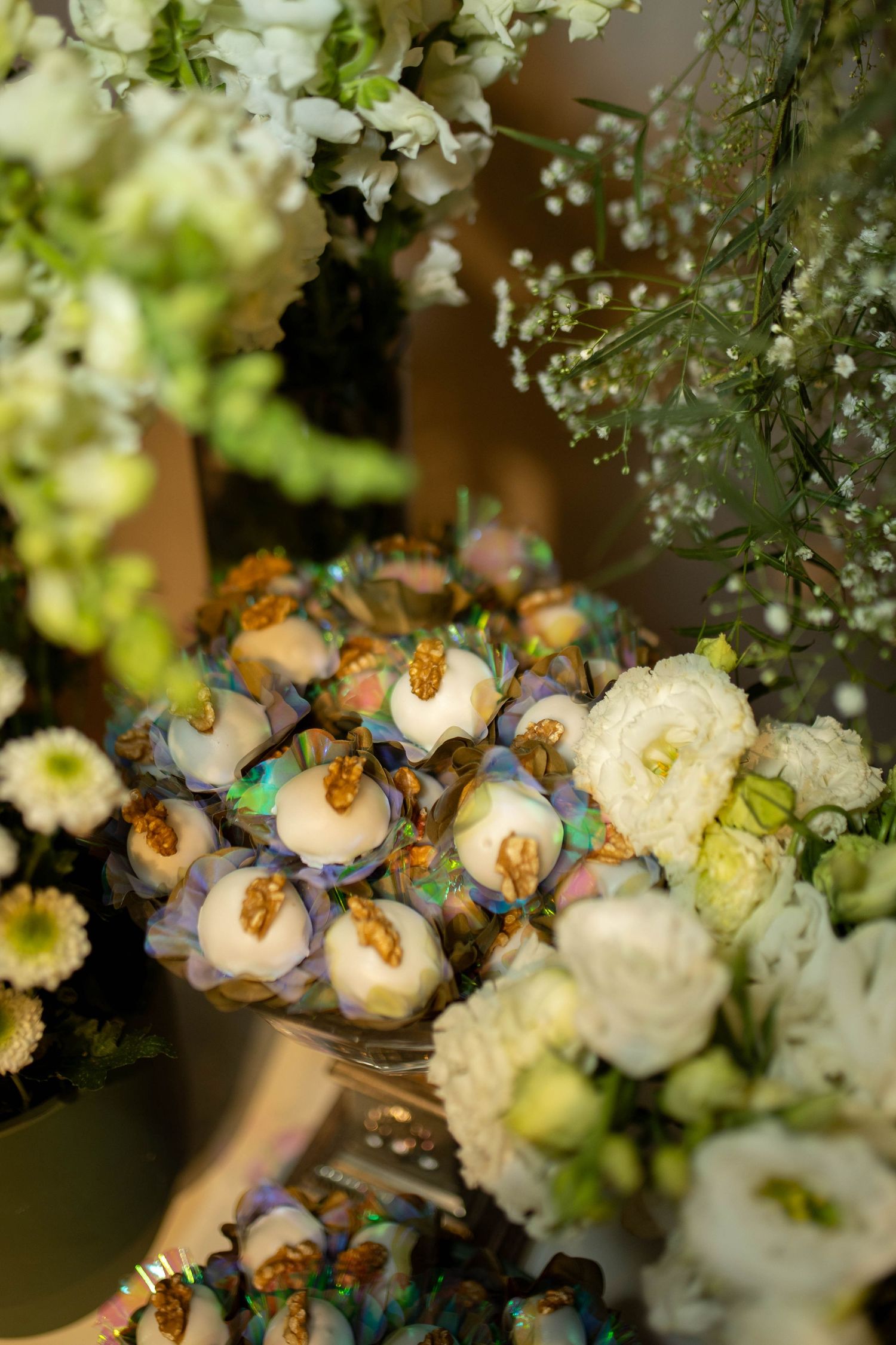 Elegant cake pops decorated with gold and purple flowers displayed among white floral arrangements at a wedding reception.