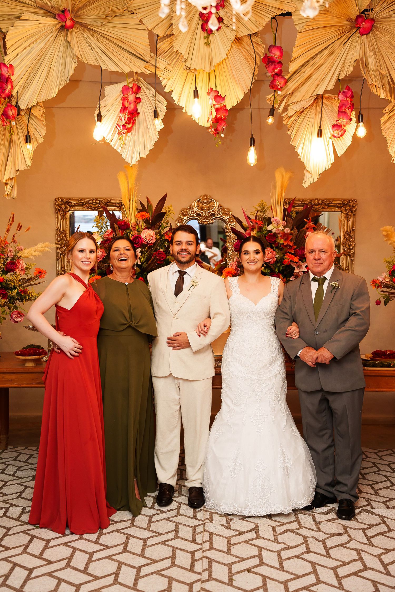 Wedding party of five posing elegantly beneath floral ceiling decor, bride in white gown flanked by family in formal attire.