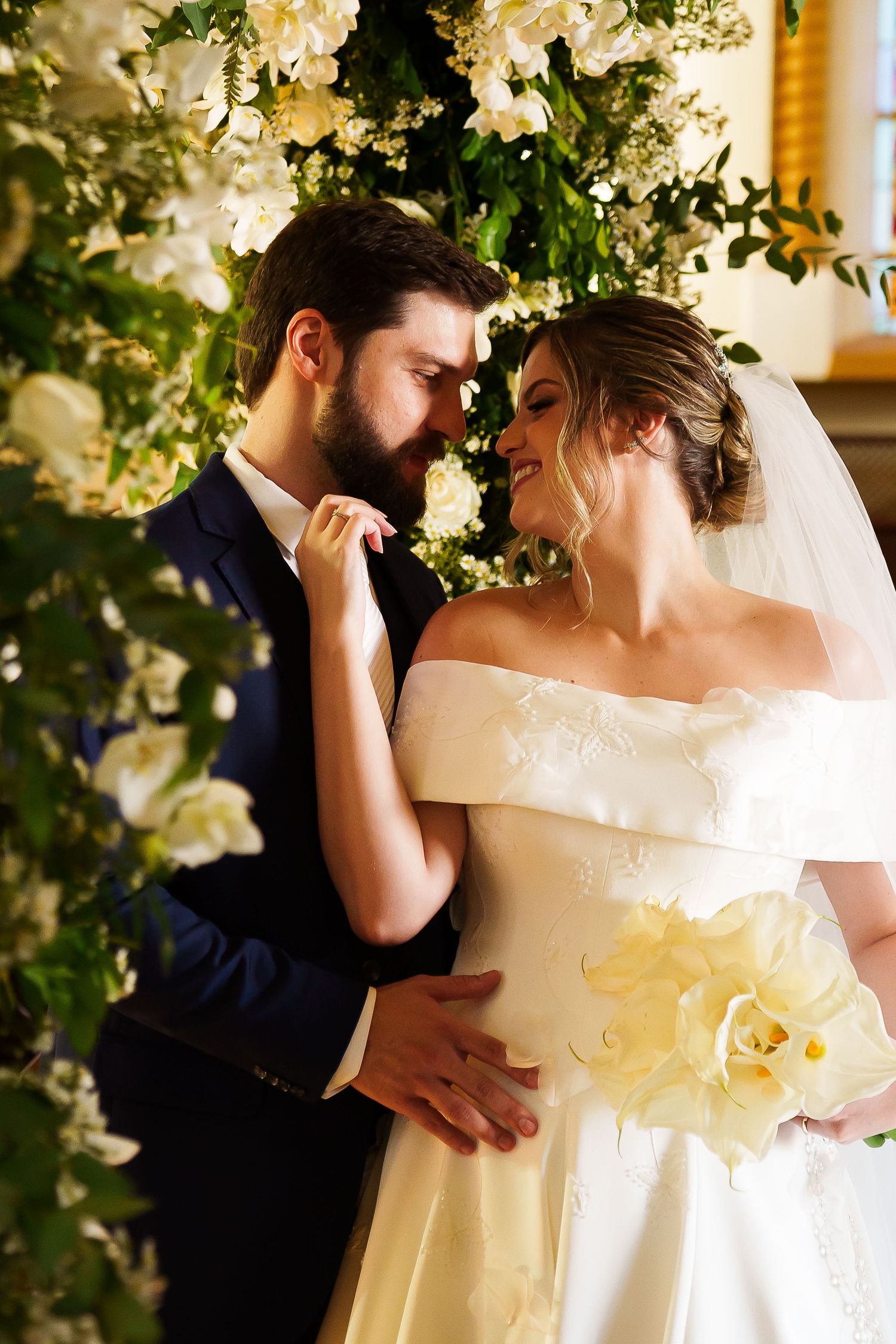 A bride and groom share a romantic moment surrounded by white floral arrangements on their wedding day.
