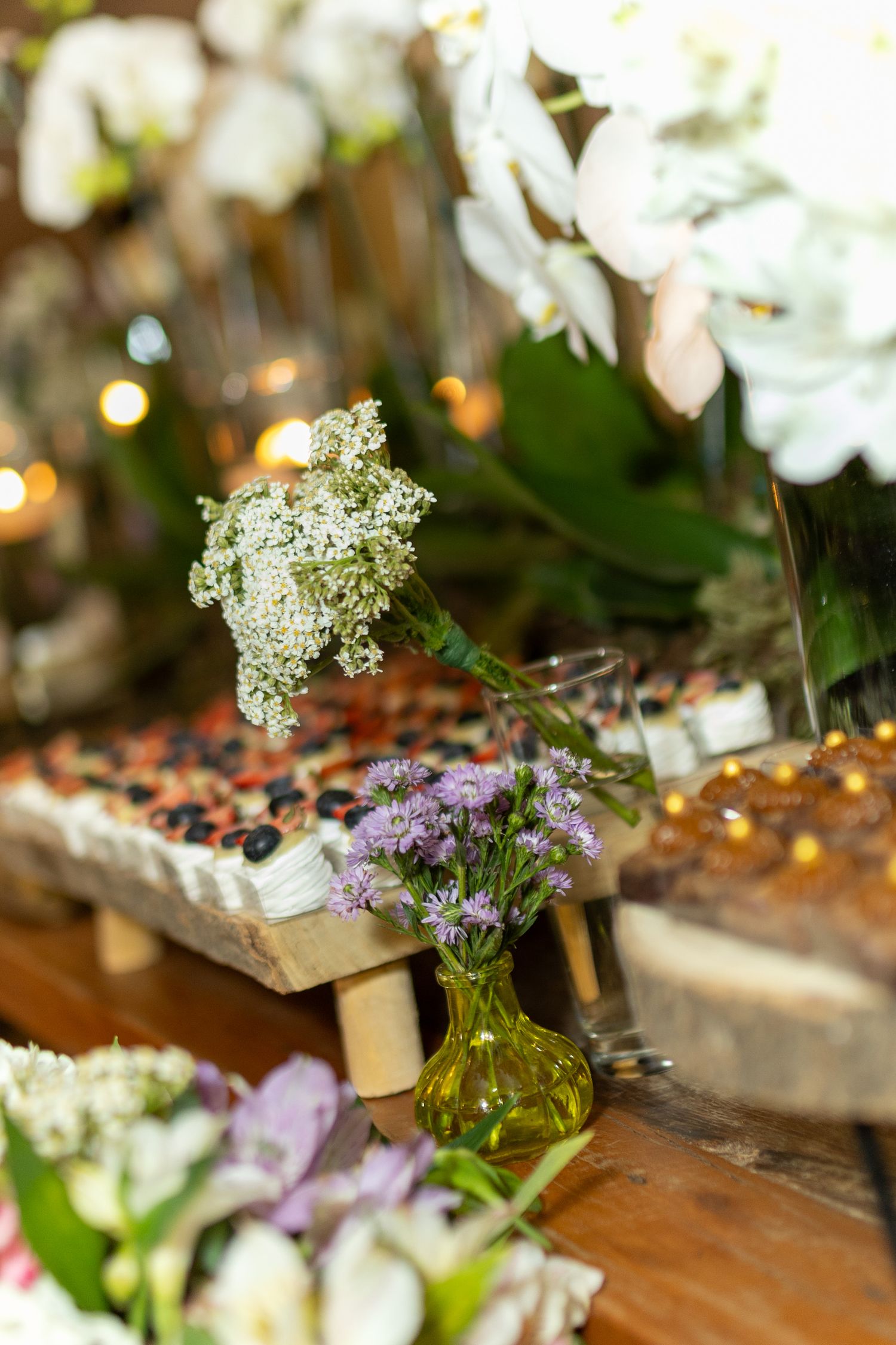 Rustic wedding table decor with small vases of white and purple wildflowers, candles, and elegant floral arrangements.
