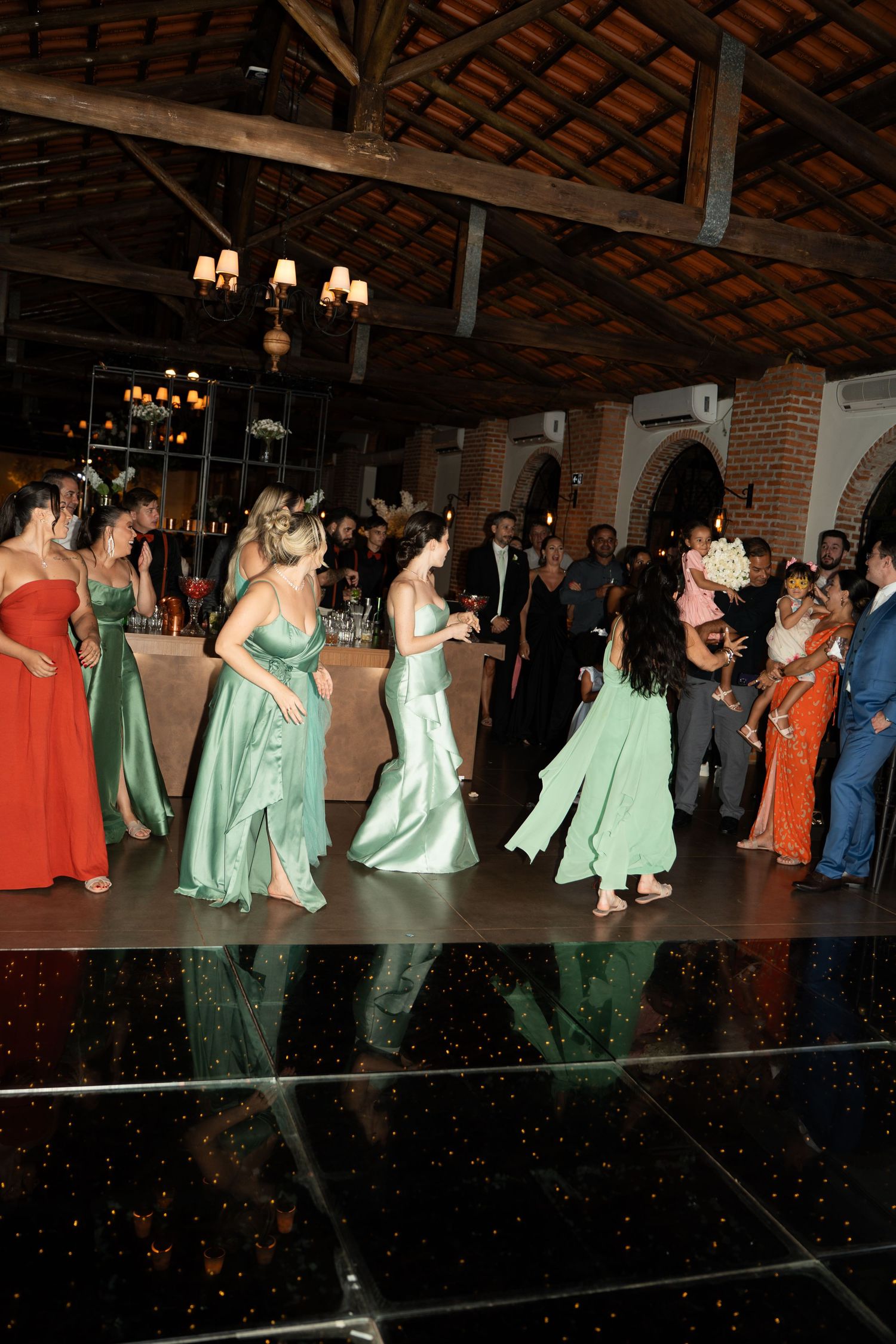 Bridesmaids in mint green gowns dancing at an elegant wedding reception on a reflective dance floor.