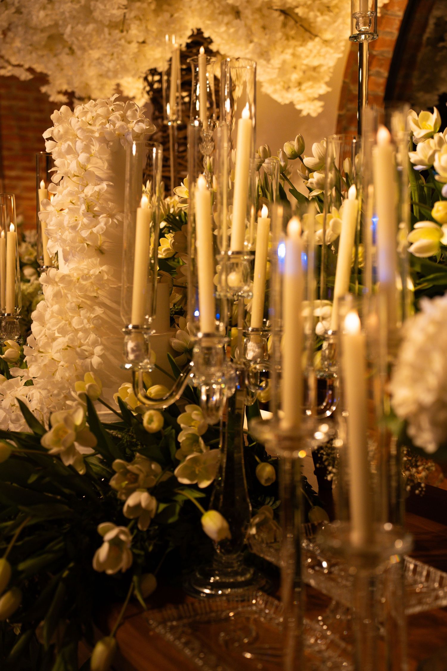 Elegant wedding candelabras with white taper candles surrounded by lush white orchids and floral arrangements.