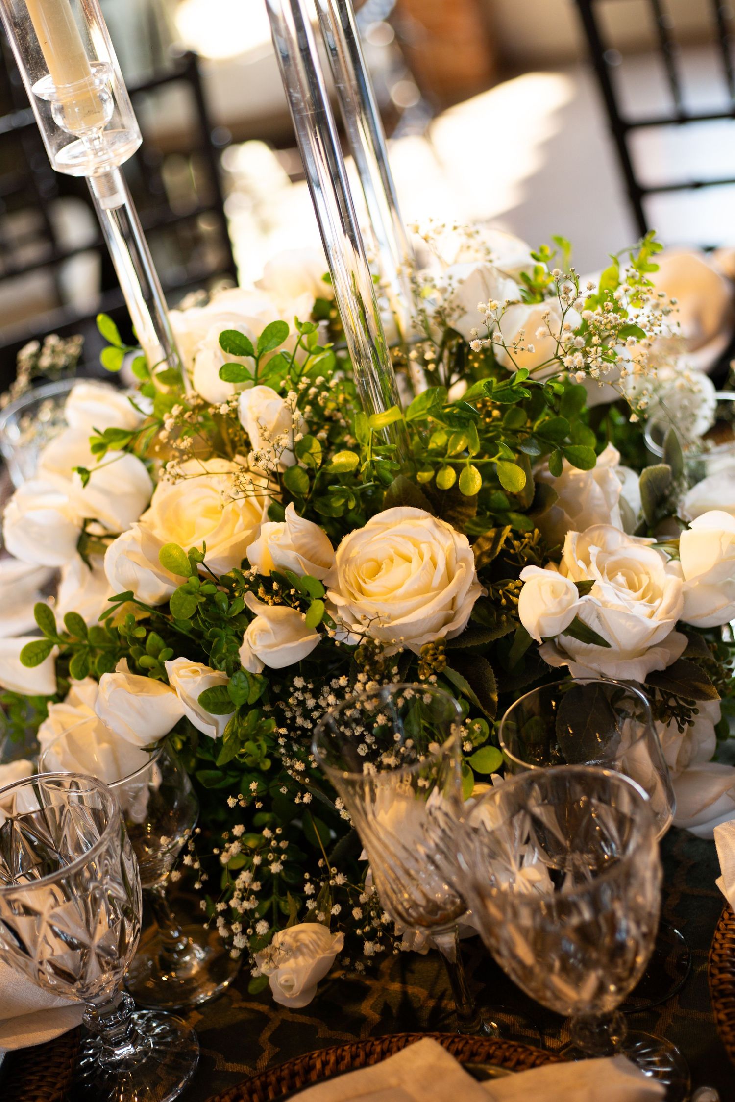 Elegant wedding centerpiece with white roses, greenery, and crystal glassware on a decorated table.