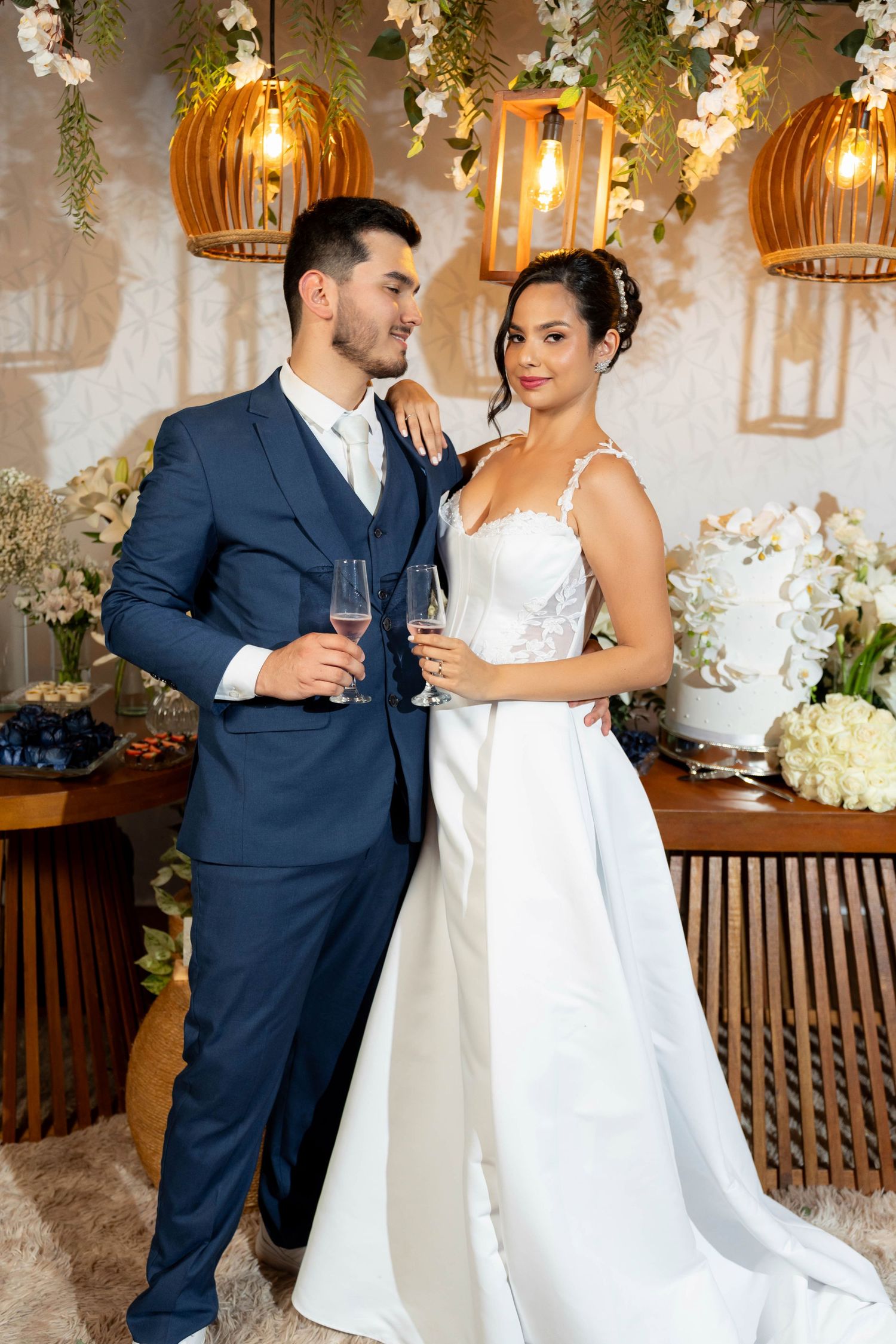 Elegant bride and groom toasting with champagne glasses at their wedding reception, surrounded by floral decorations and warm lighting.