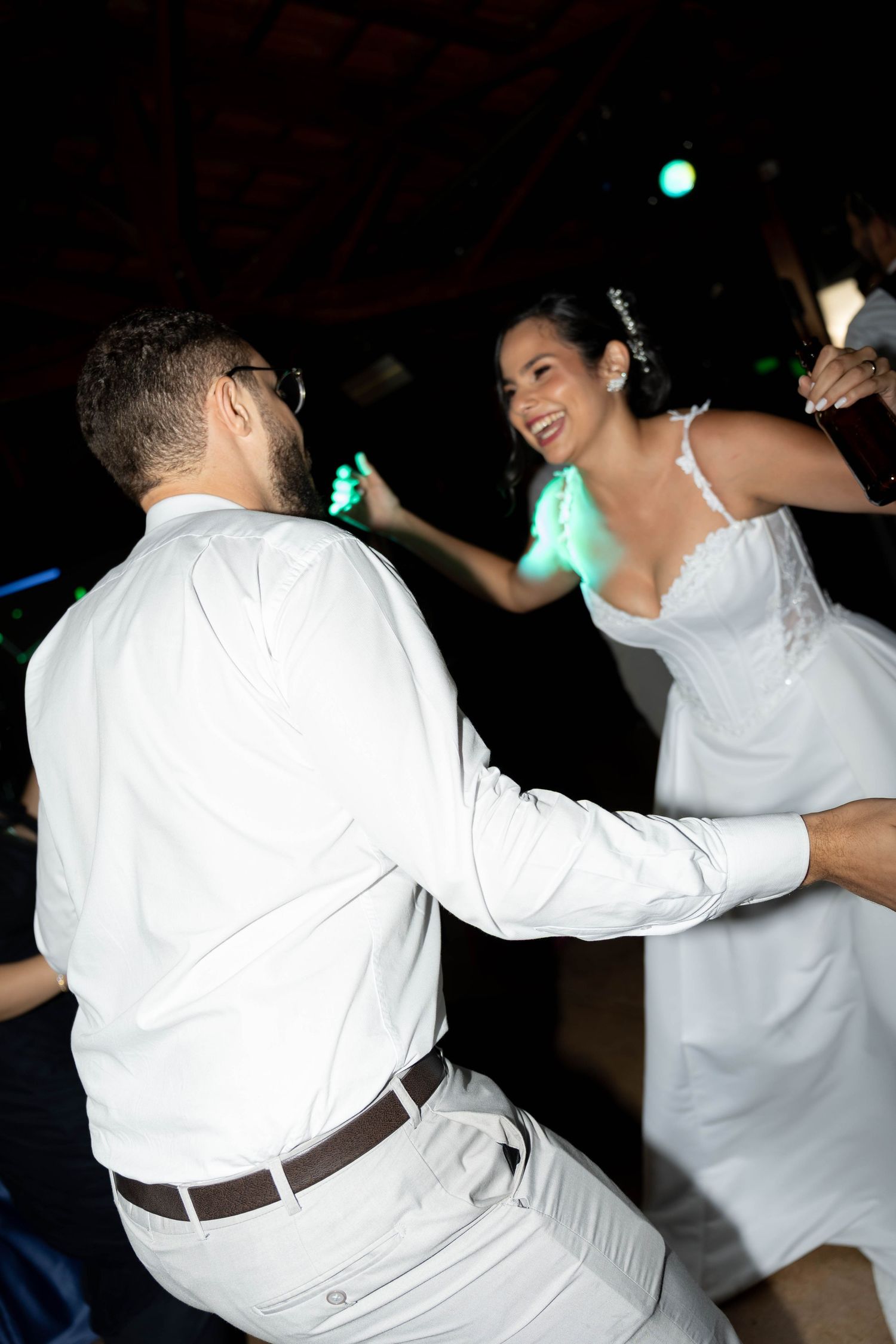 Bride and groom dancing joyfully at their wedding reception, woman in white dress laughing.