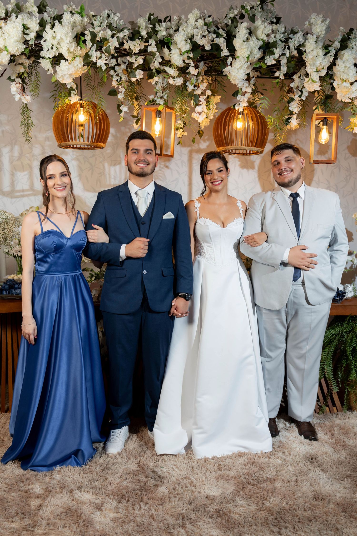 Wedding party of four posing elegantly under floral decorations and warm pendant lights in a beautifully decorated venue.