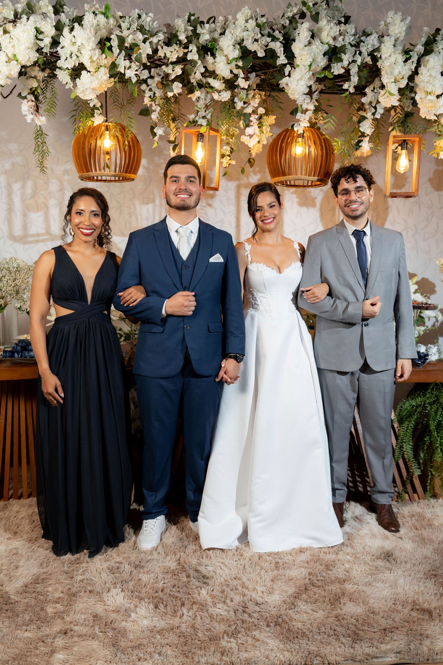 Bride and groom pose with two guests under floral ceiling decor and warm pendant lights at elegant wedding reception.