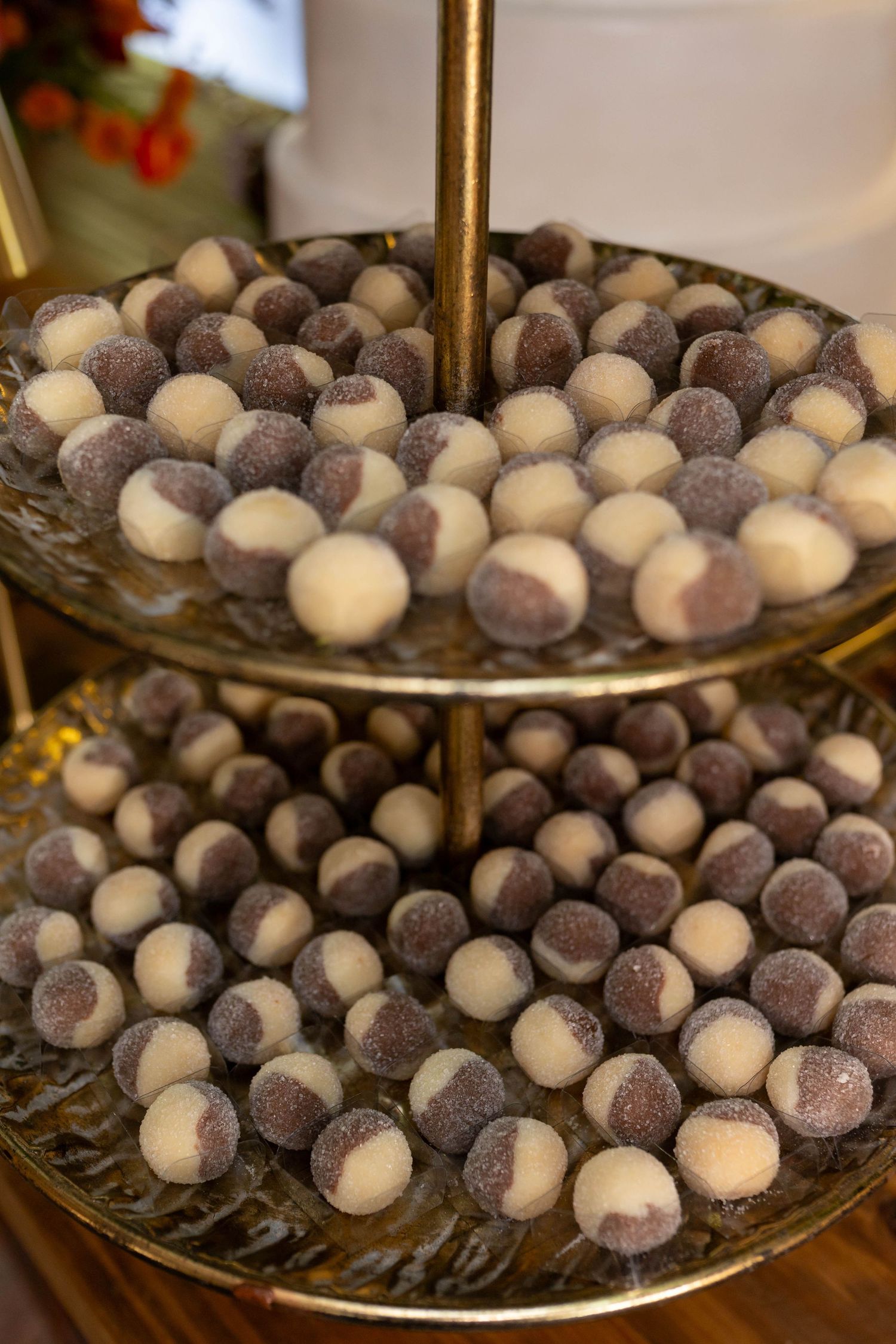 Two-tiered gold stand displaying rows of white and sugar-coated chocolate truffle balls at a dessert display.