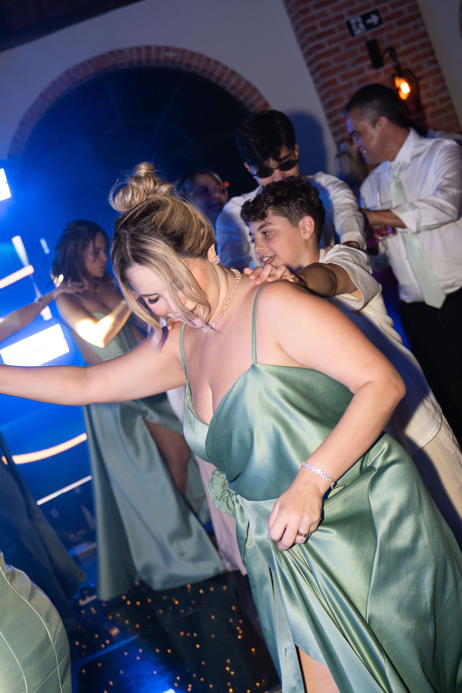 Young woman in green satin gown dancing at a formal event with guests and blue lighting in background.