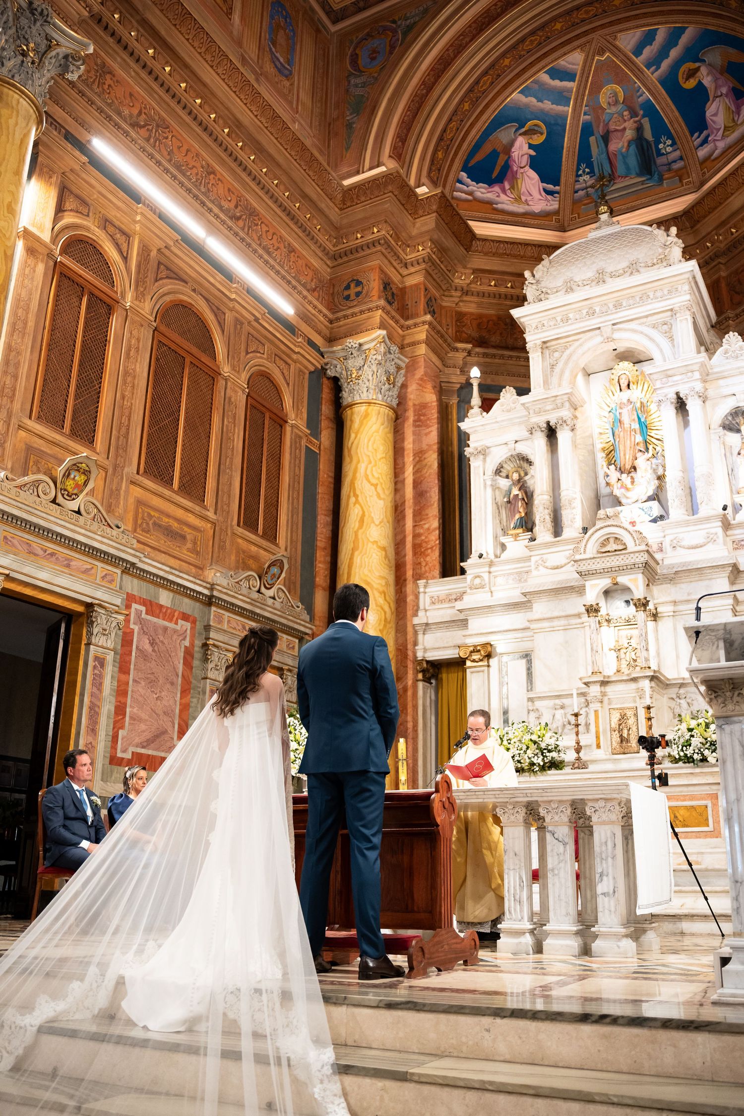 Bride and groom stand before ornate marble altar during Catholic wedding ceremony in elegant historic church.