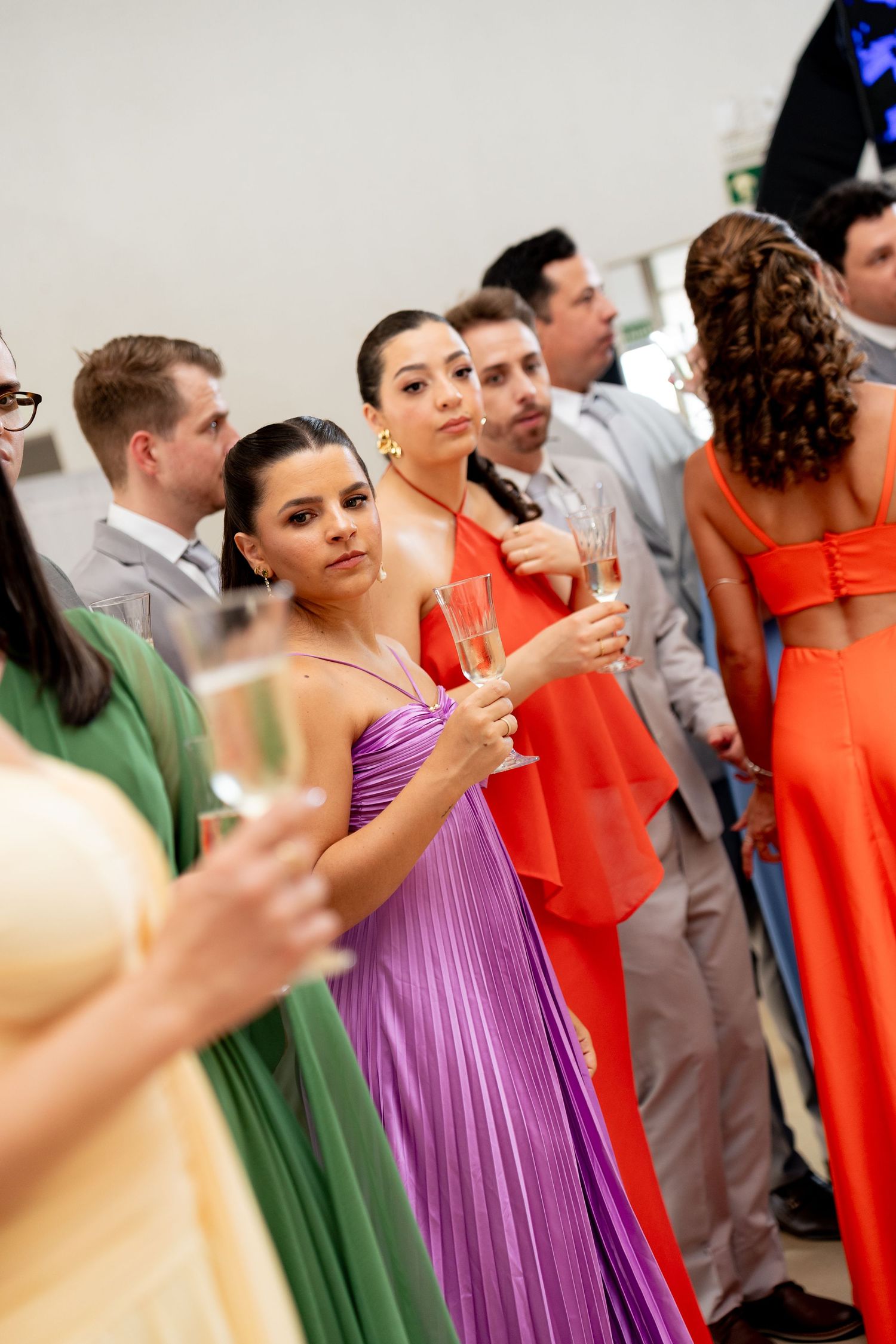 Elegantly dressed guests in colorful gowns holding champagne glasses at a formal event or gala.