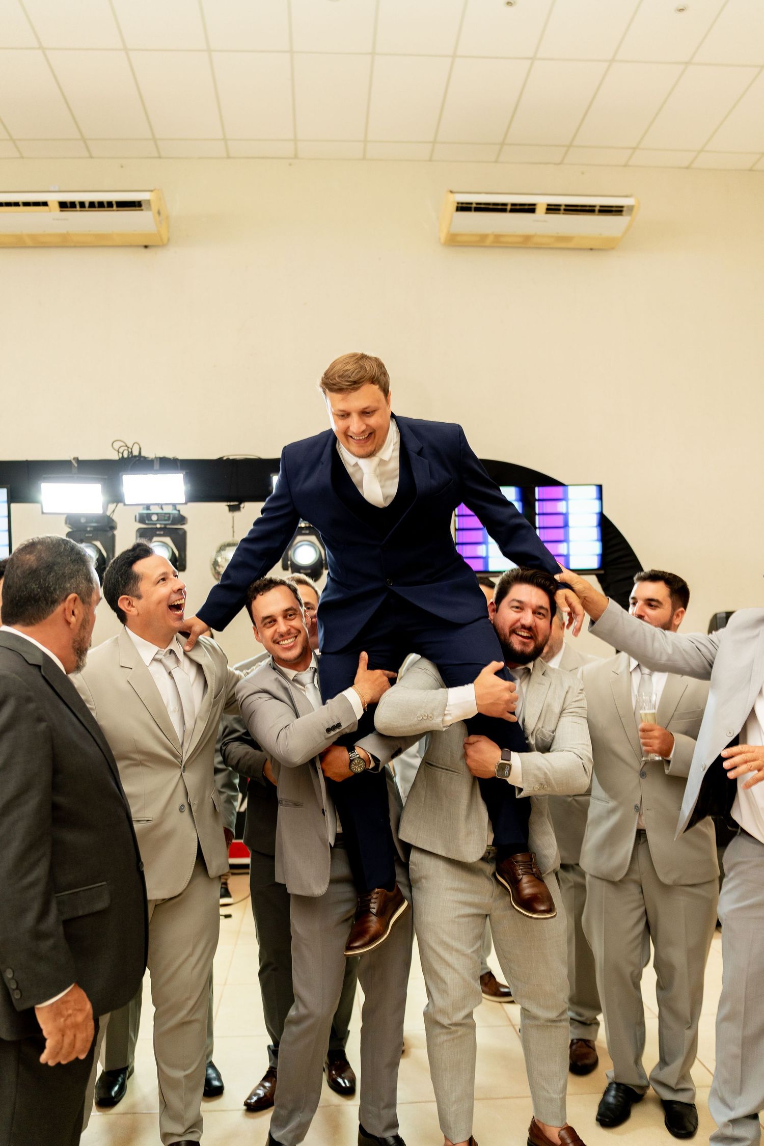 Groomsmen lifting groom in navy suit during wedding celebration in banquet hall.