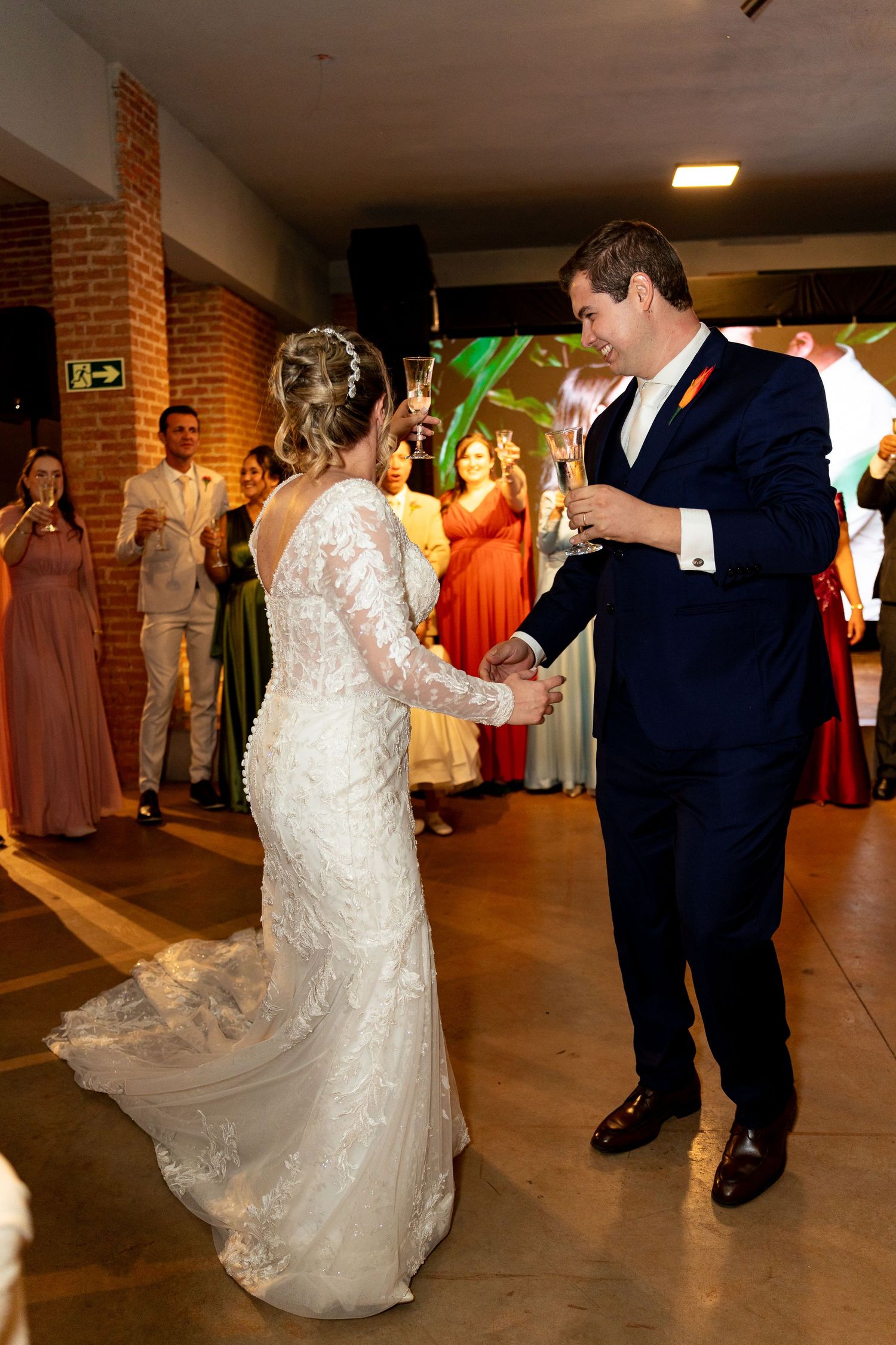 Bride and groom share their first dance at wedding reception, bride in lace gown, groom in navy suit.