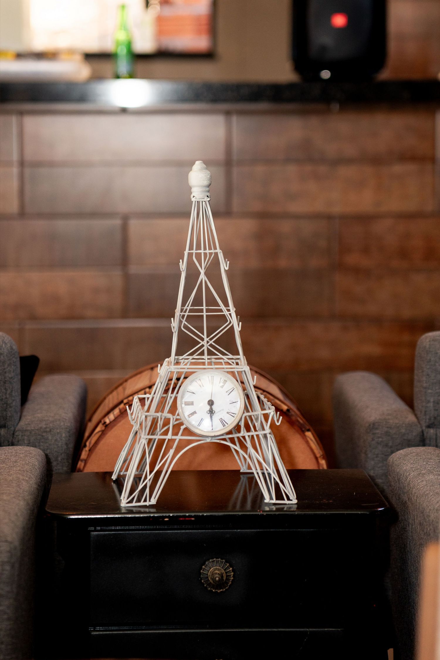 White wire Eiffel Tower clock sculpture displayed on a black table between gray chairs in a modern interior.
