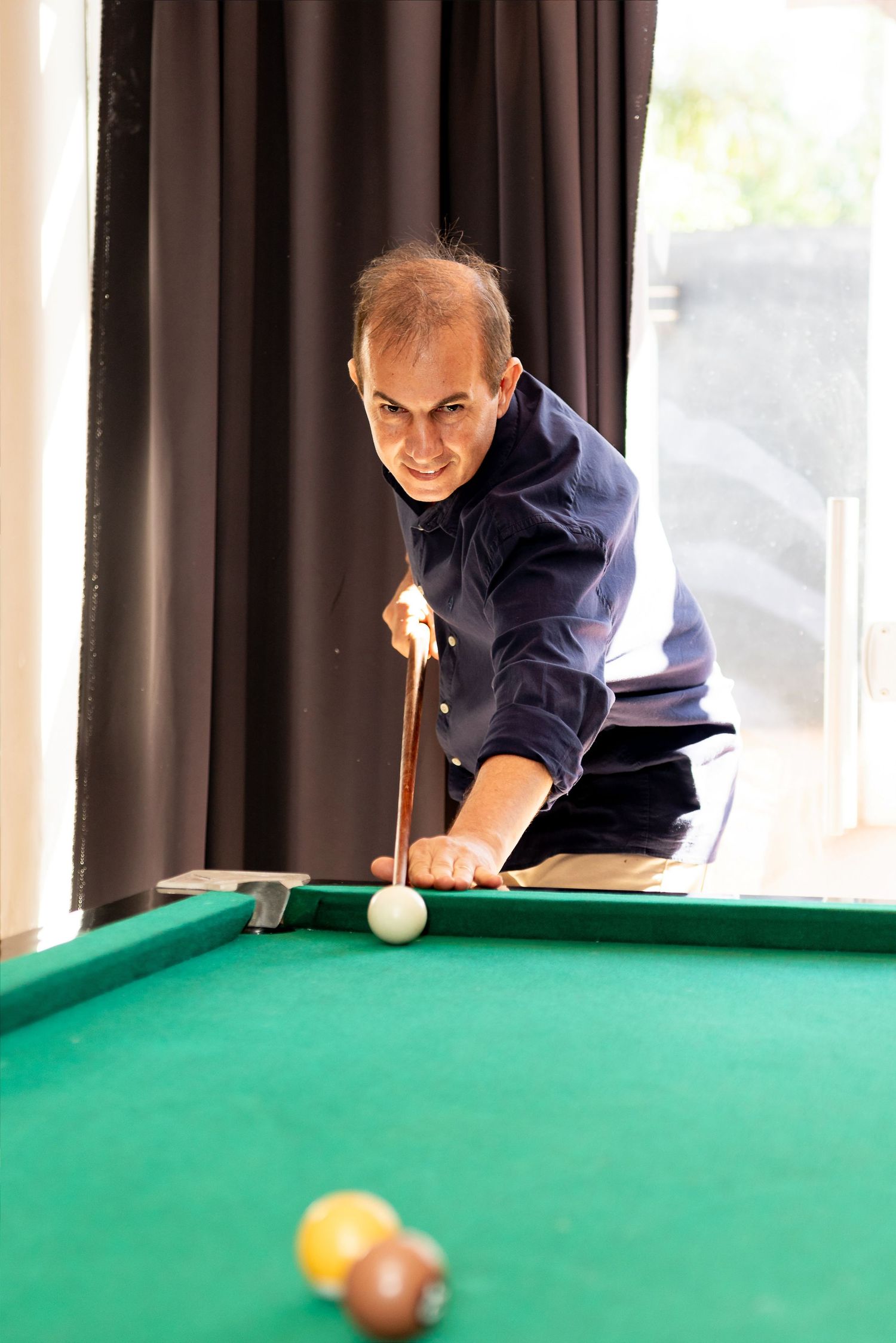 A man leaning over a green pool table, aiming his cue stick at the white ball during a game of billiards.