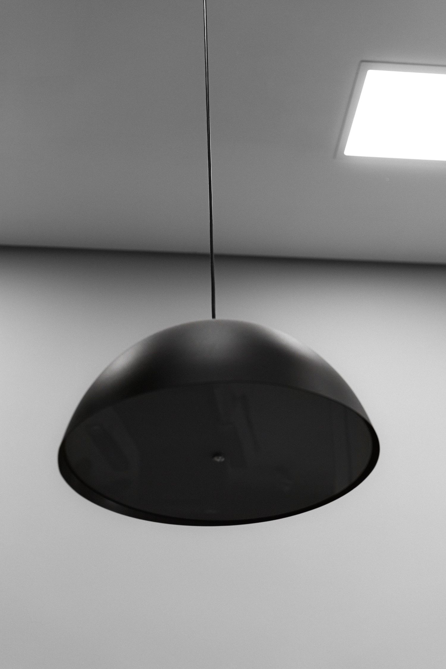 Modern black dome pendant light hanging from ceiling with square skylight in monochrome interior.