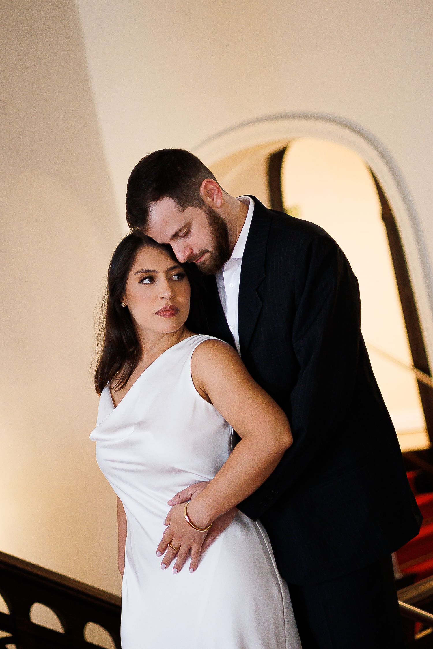 Elegant couple in formal wear embracing on a staircase, woman in white dress, man in black suit.