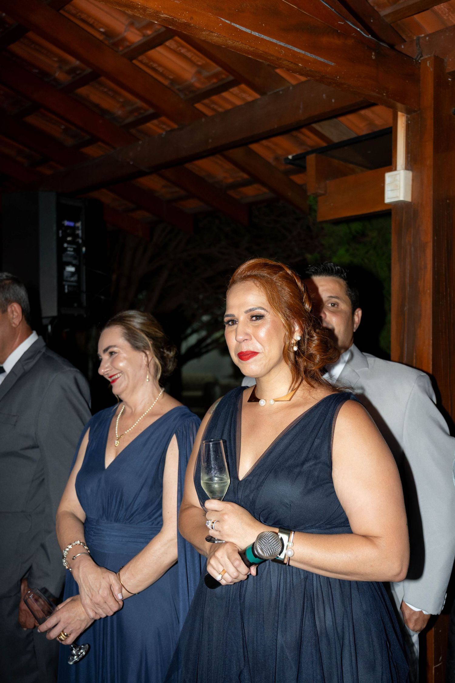 Two women in matching navy blue gowns holding champagne glasses at an elegant evening event.
