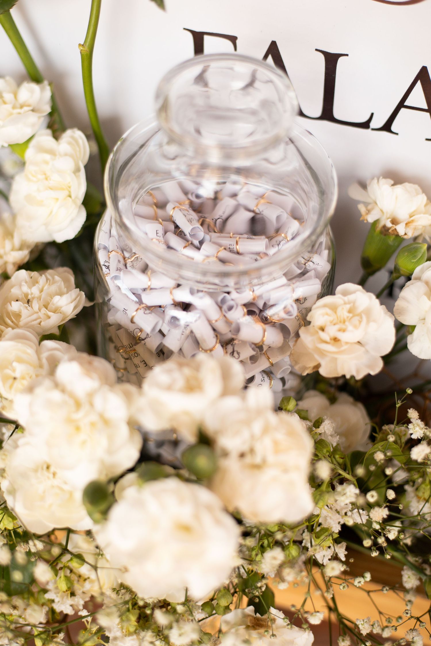 Glass jar filled with rolled paper notes surrounded by white carnations and baby's breath flowers at a wedding.