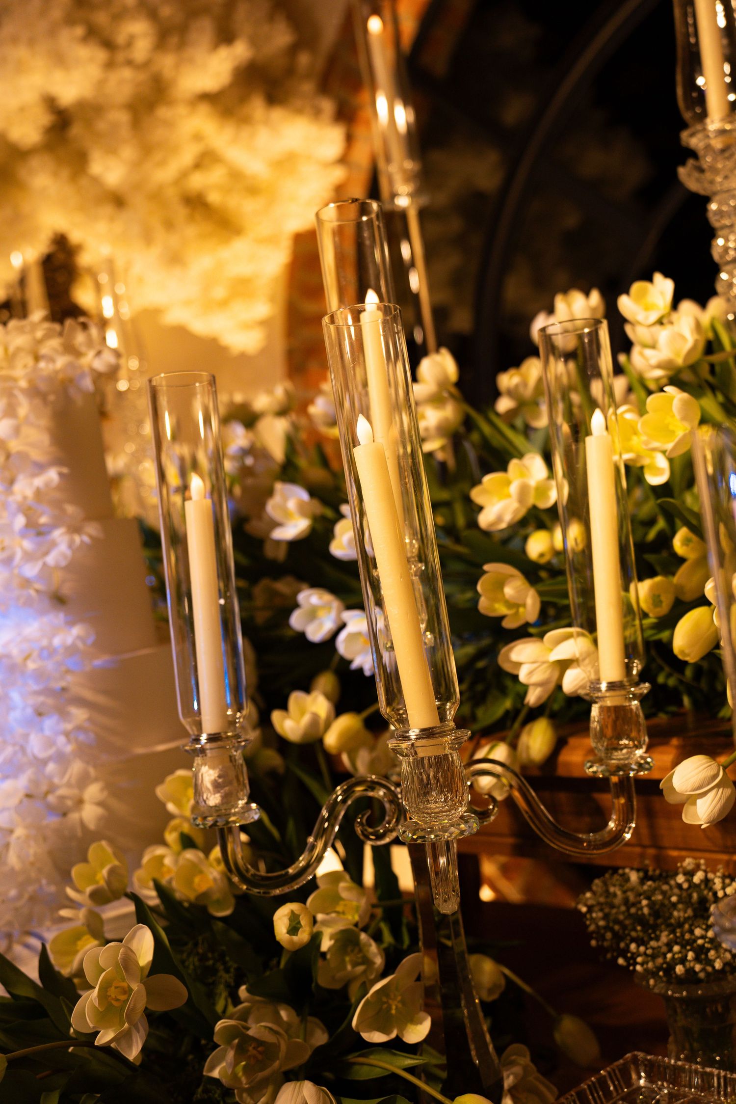 Elegant crystal candelabra with white taper candles surrounded by yellow and white flowers at a wedding reception.