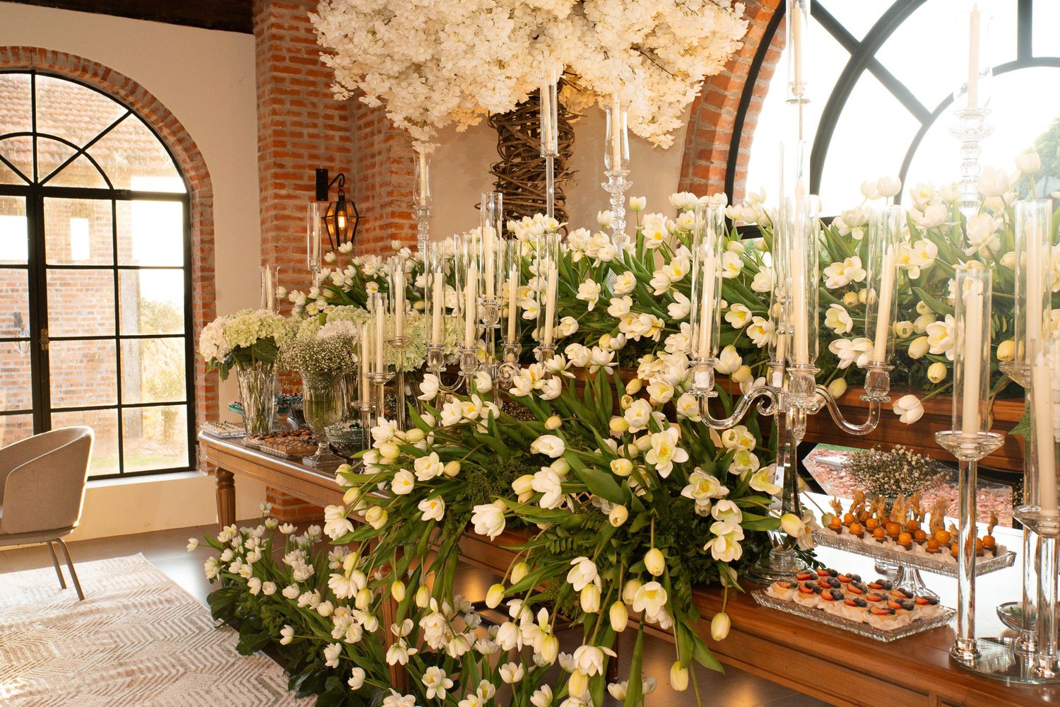 Elegant floral display with white roses and tall candelabras in a rustic brick venue with arched windows.