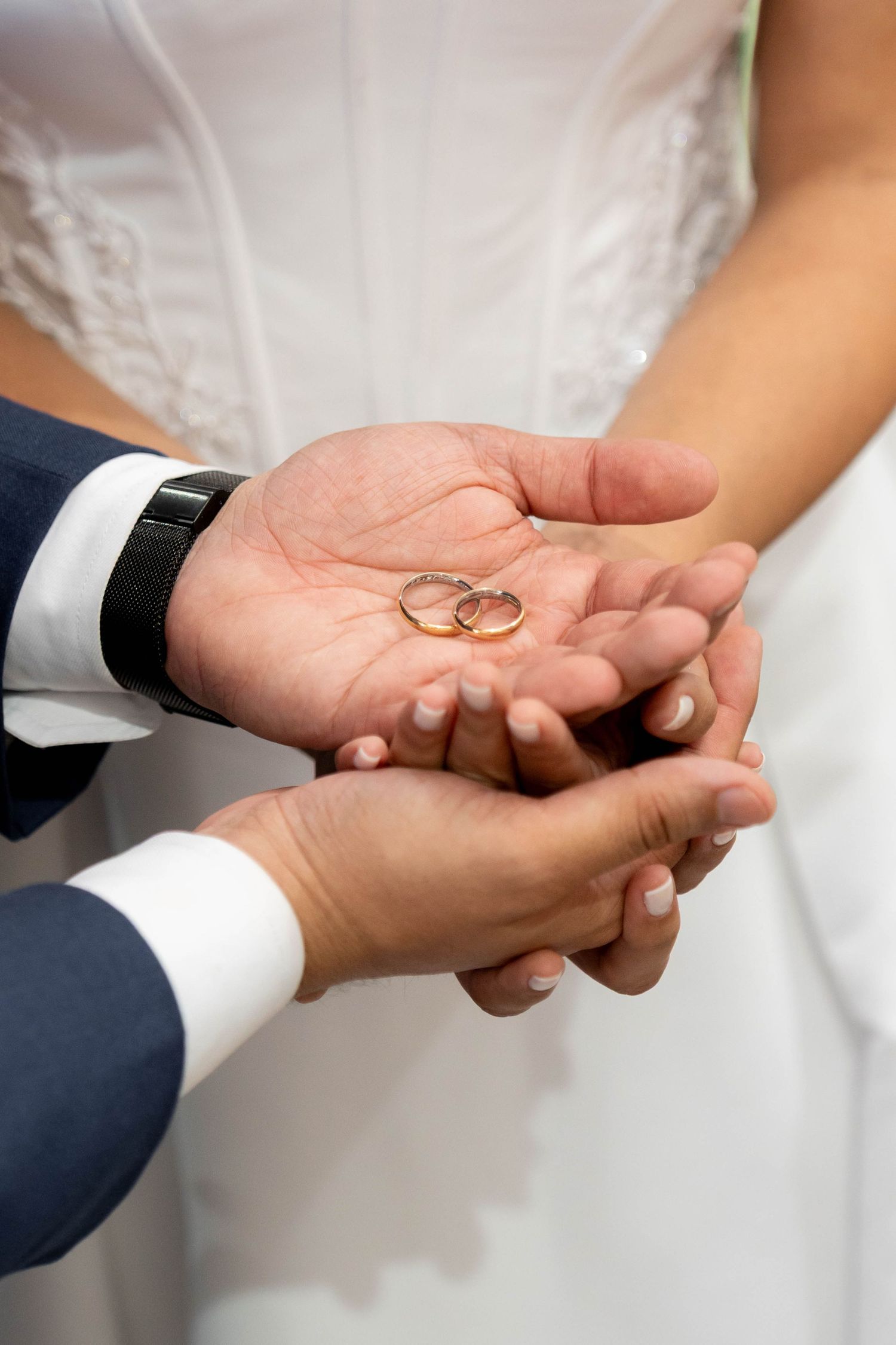 Couple holding two gold wedding rings in their joined hands during a wedding ceremony.