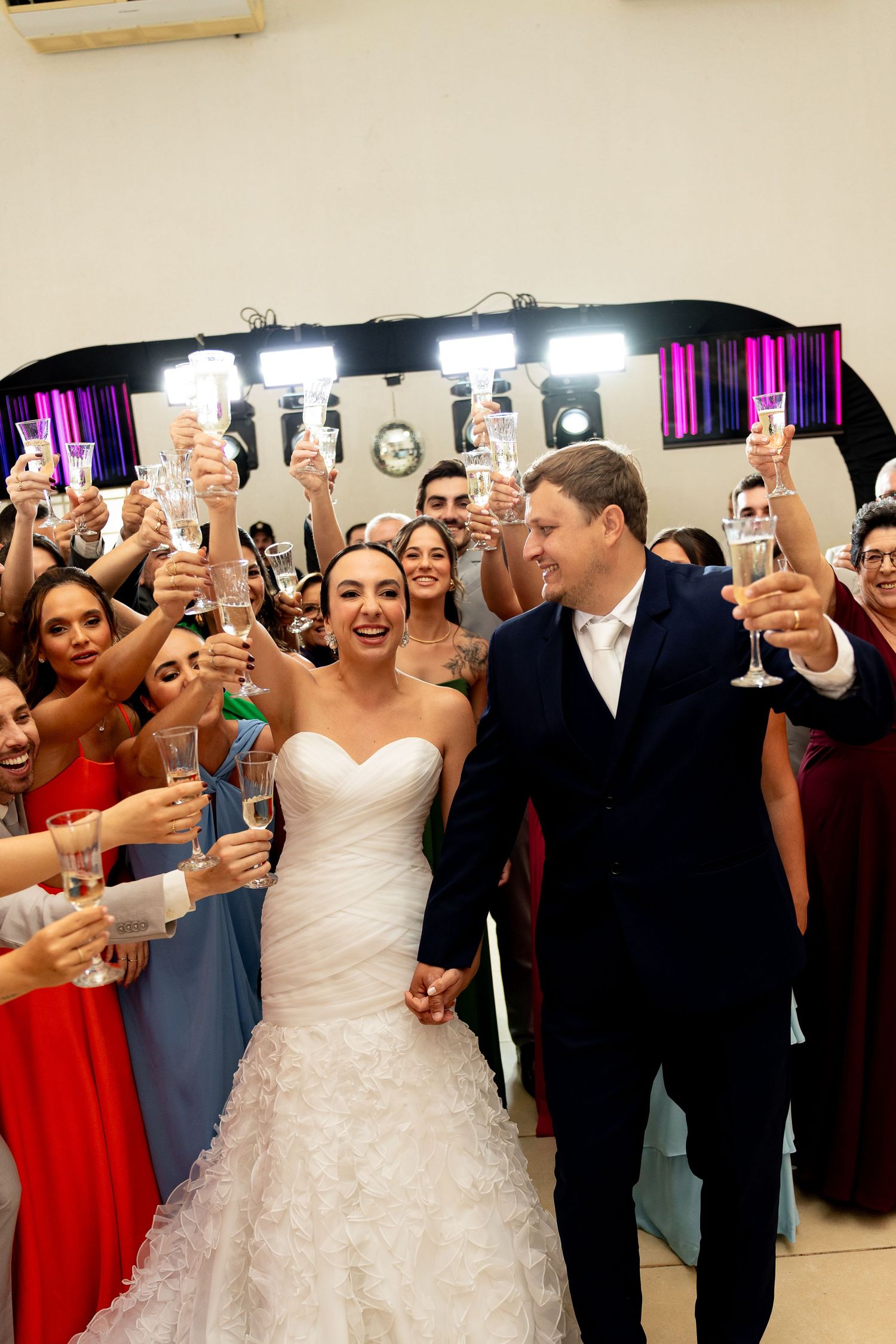Bride and groom walk hand-in-hand as wedding guests raise champagne glasses in celebration at their reception.