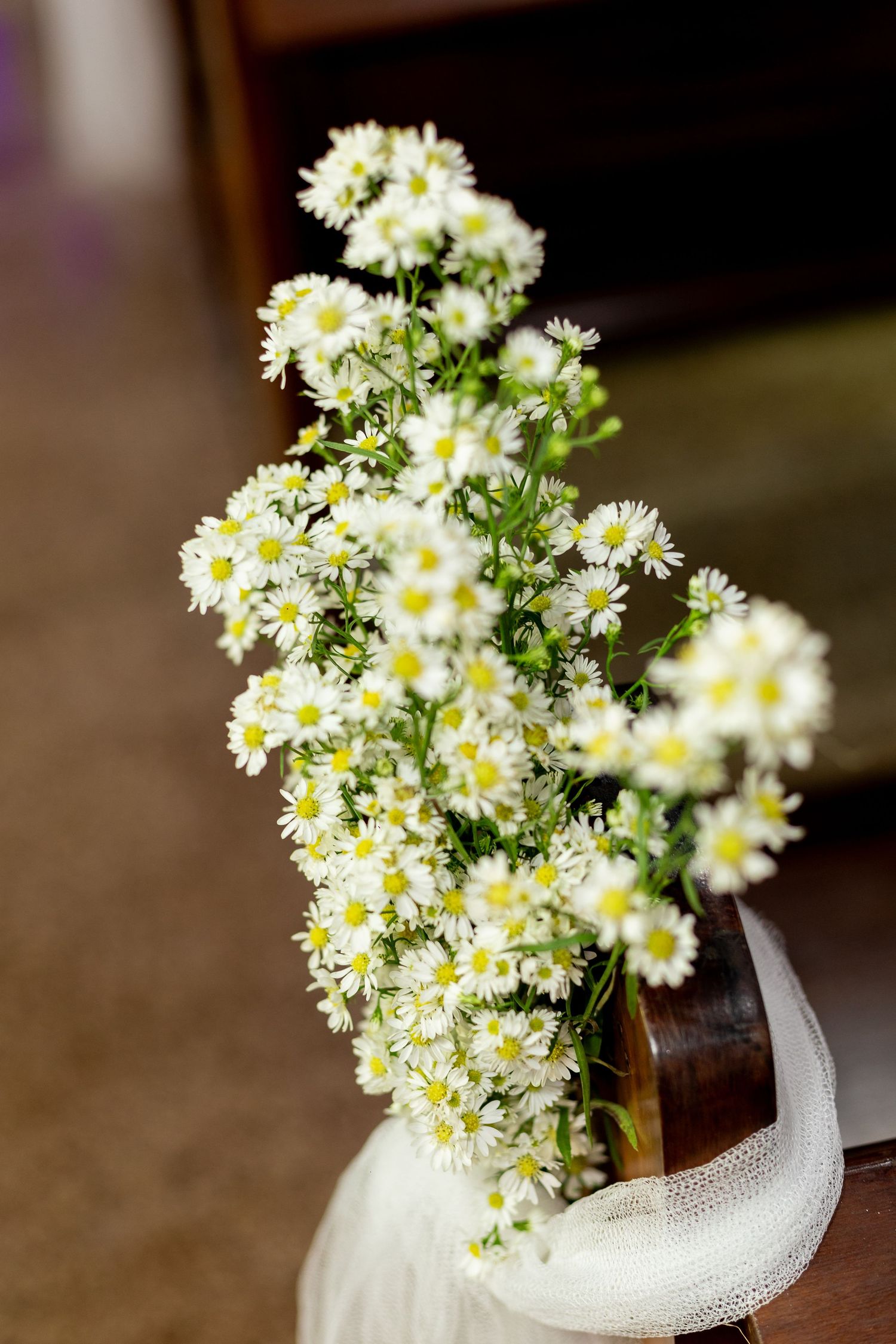 Small white daisy bouquet in a glass vase with white tulle, perfect for a wedding ceremony decoration.