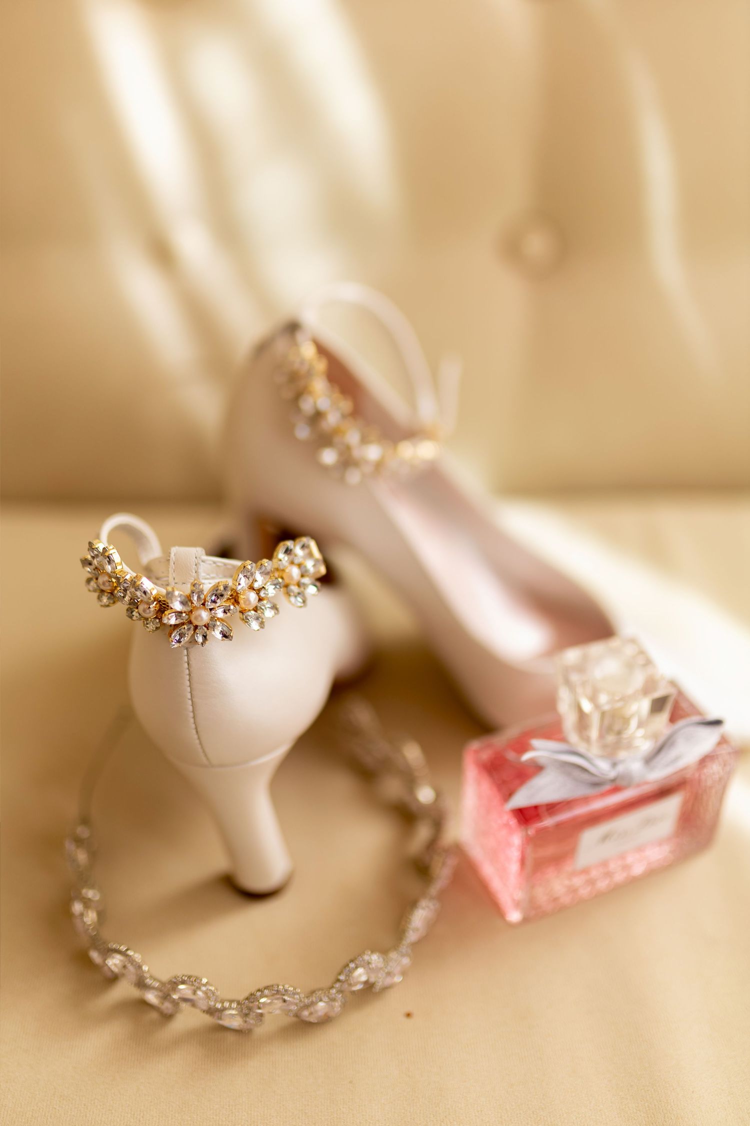 Elegant bridal accessories featuring blush pink heels adorned with gold jewelry, a crystal necklace, and a pink Dior perfume bottle.