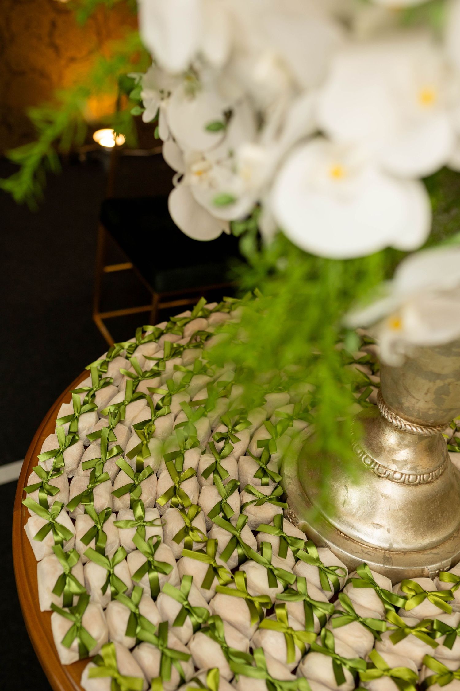 Elegant wedding favor display with white ribbon-tied treats on wooden tray beside silver vase with white orchids.
