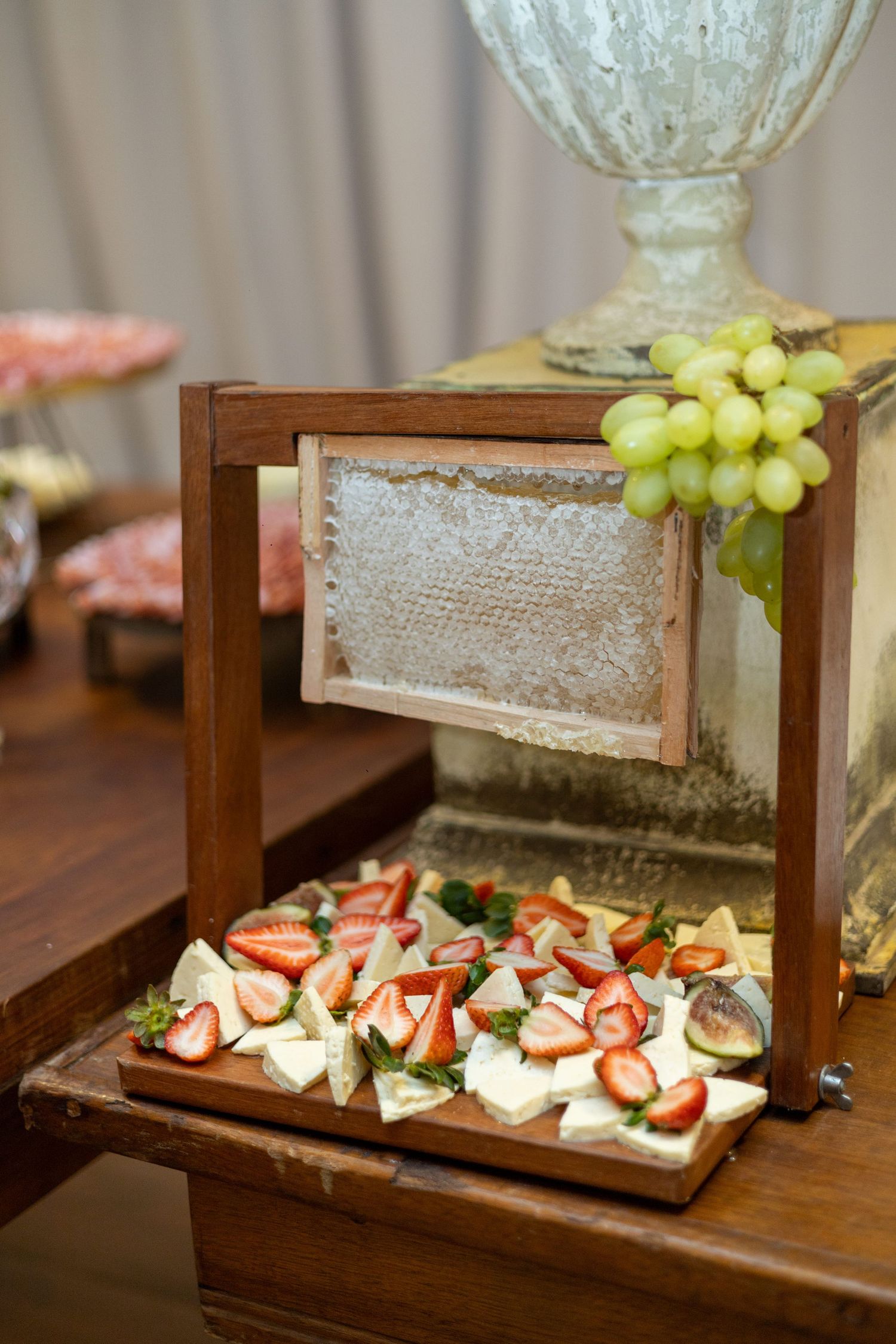Elegant wooden display box with fresh strawberries, figs, and cheese bites, topped with green grapes at a catered event.