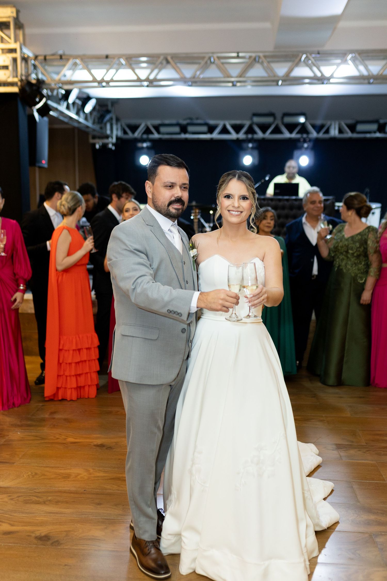 Bride and groom posing with champagne glasses at their elegant wedding reception with guests in background.