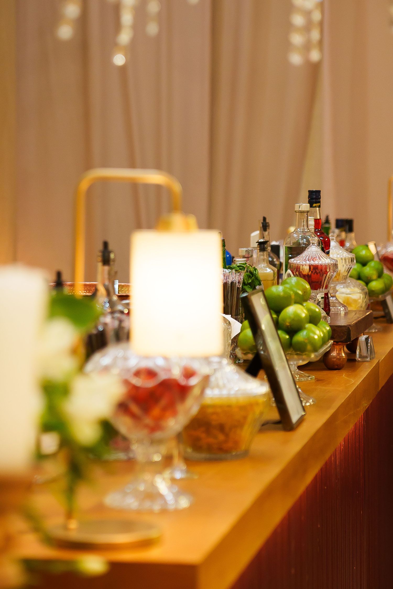 Elegant bar setup with glowing lamp, green apples, bottles, and crystal bowls at a catered event.
