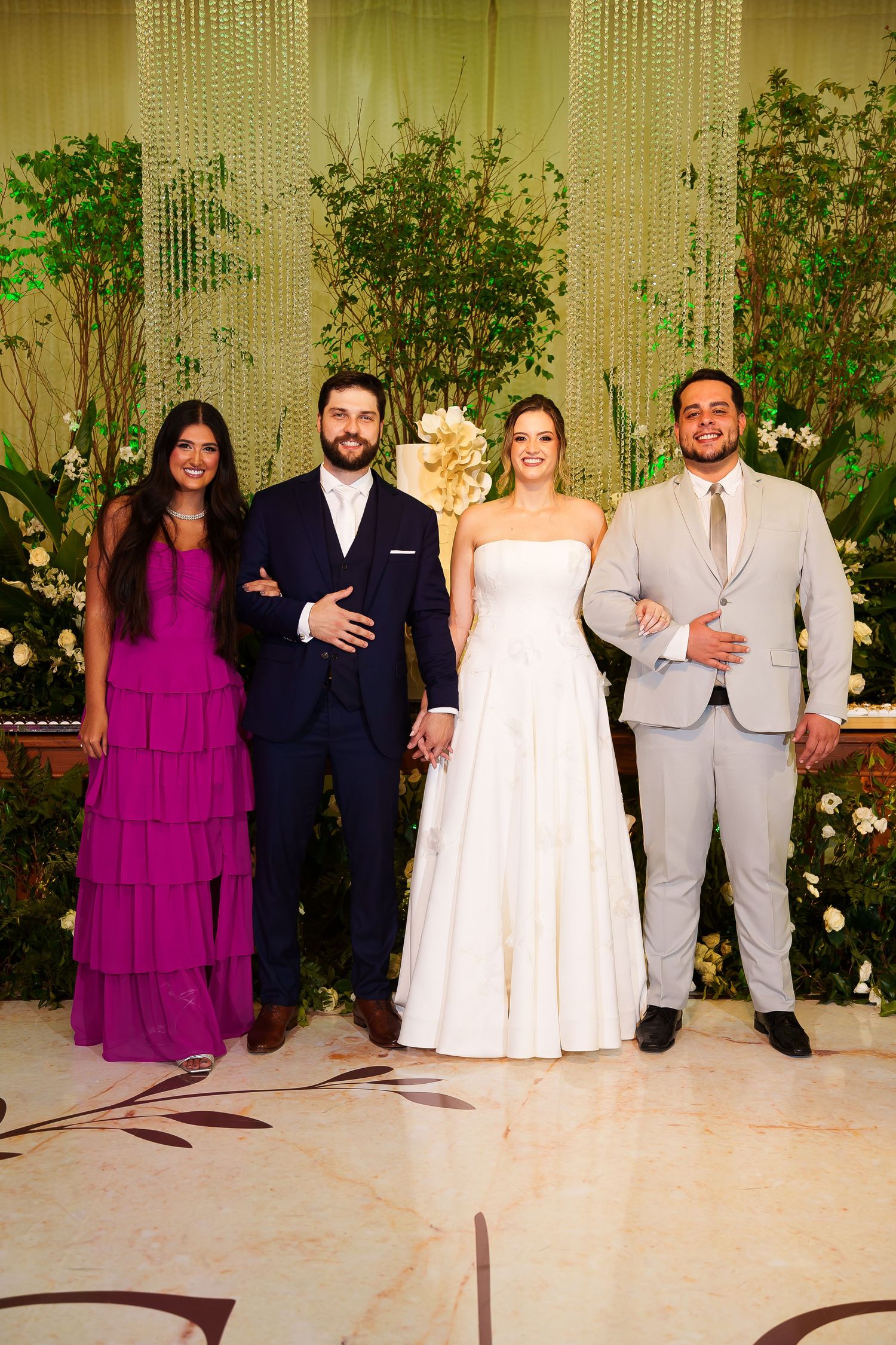 Wedding party of four posing elegantly, bride in white gown, groom in navy suit, guests in magenta dress and gray suit.