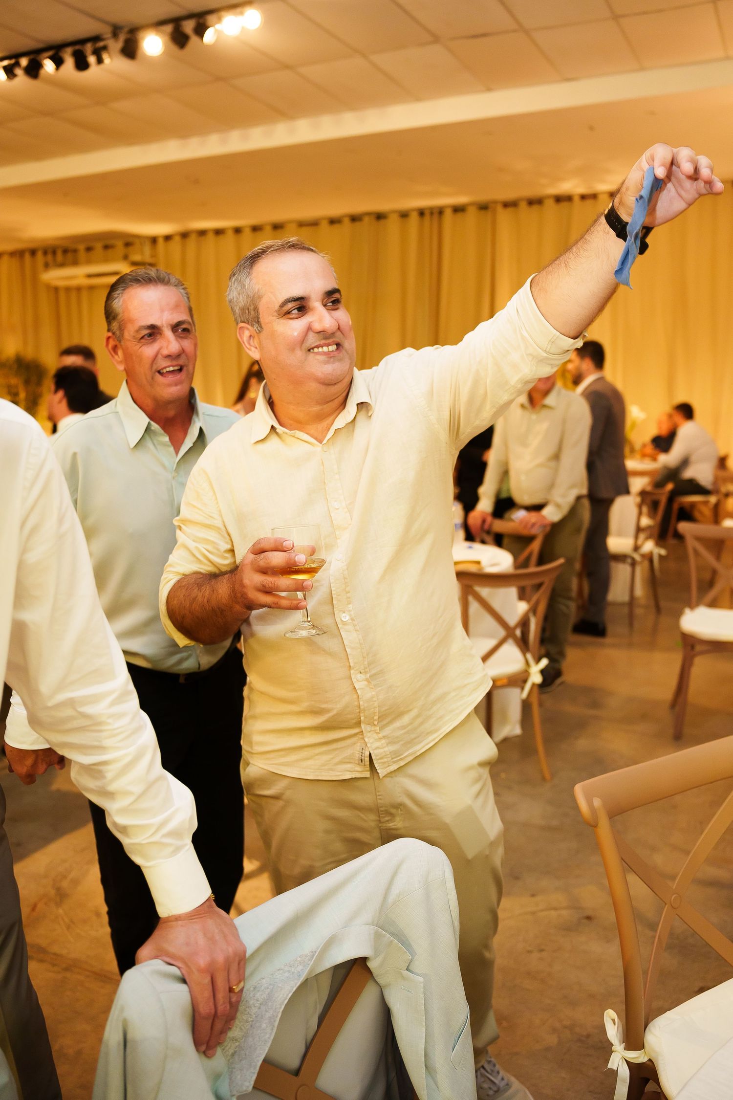 Man in yellow shirt taking a selfie while holding a drink at an indoor event or celebration.