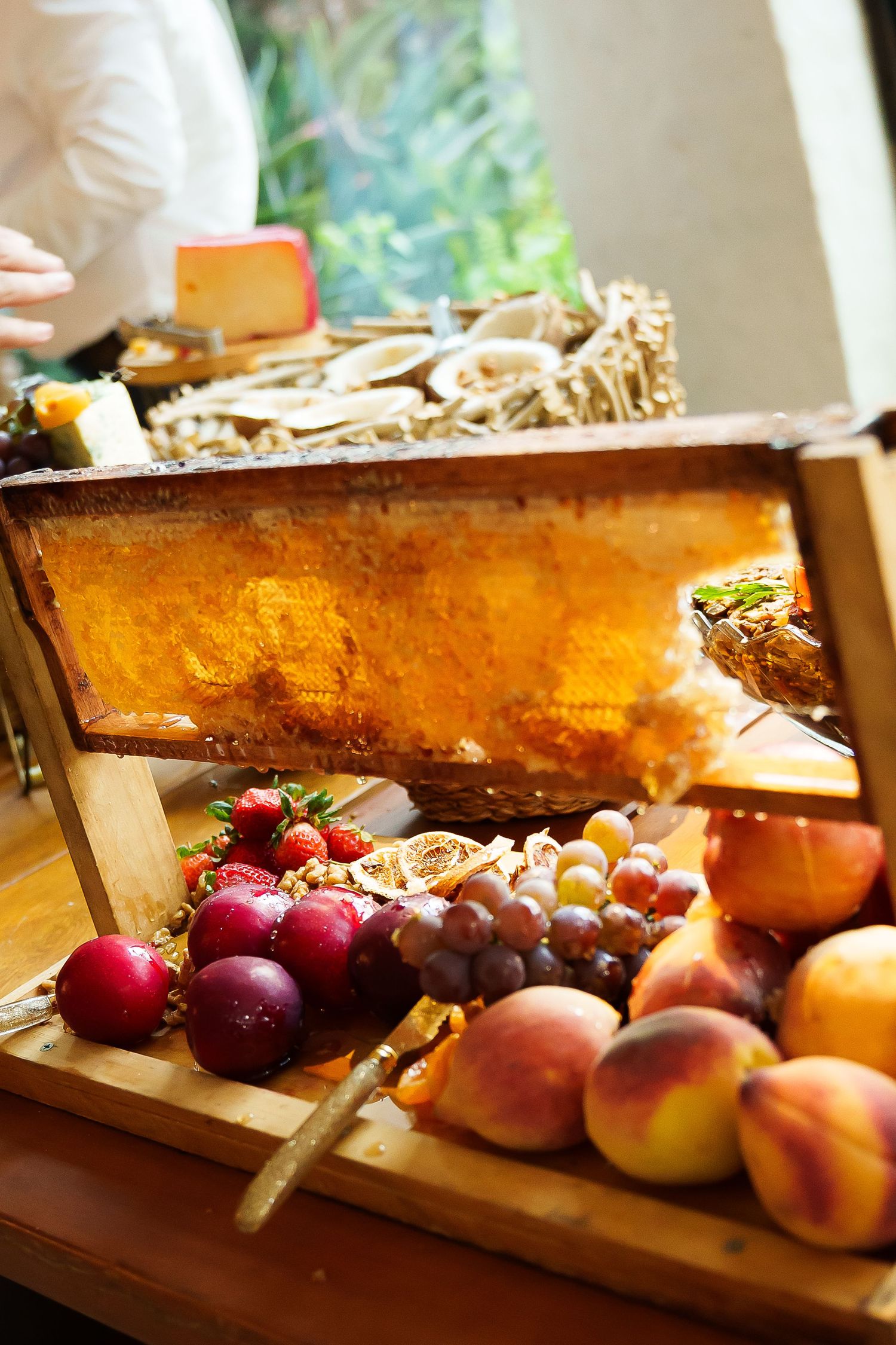 A rustic wooden display with honeycomb, fresh fruits including grapes, peaches, and strawberries at an elegant catering event.